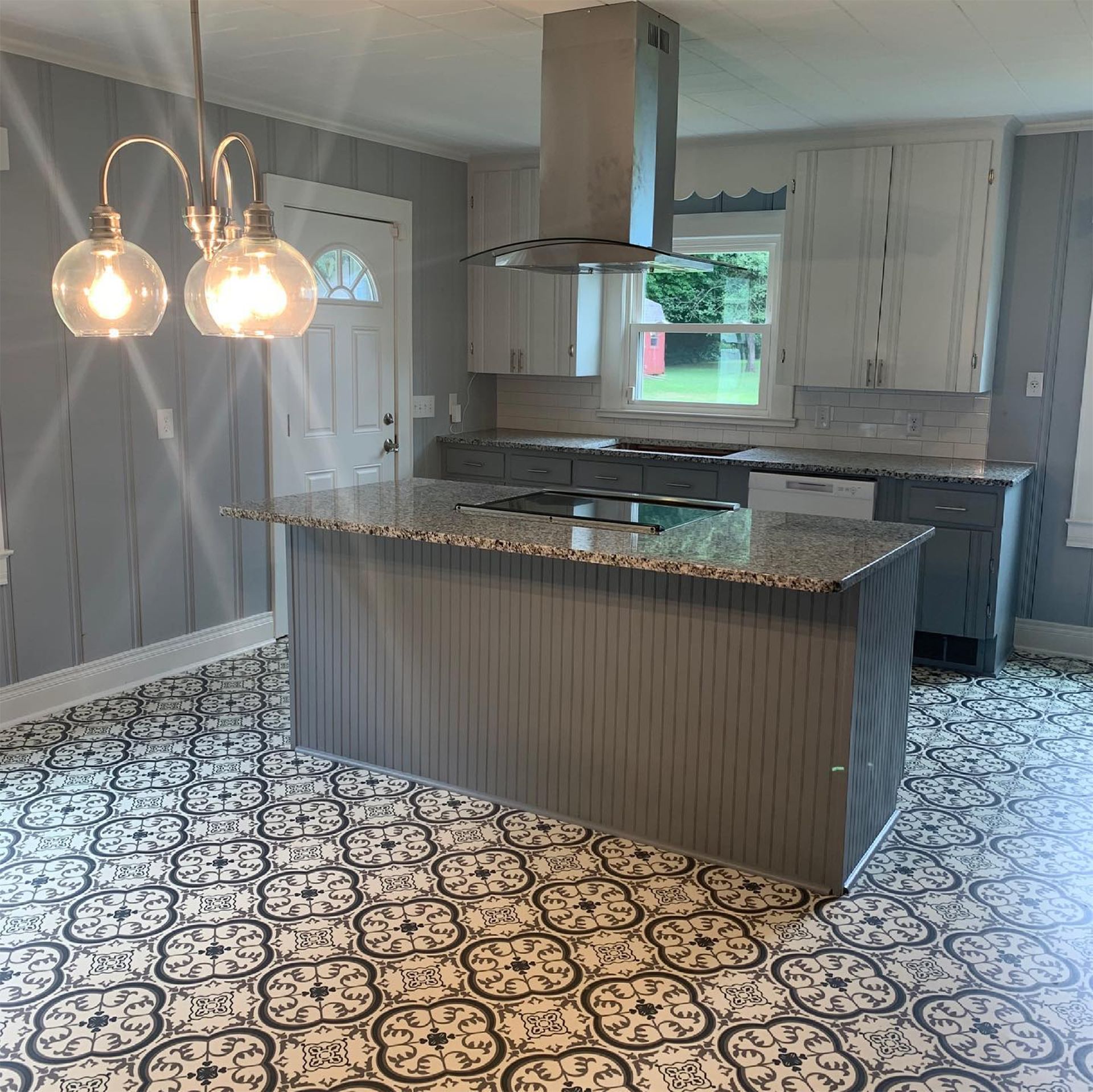 Kitchen with a gray island, cabinets, patterned floor, stainless steel hood, and pendant lights.