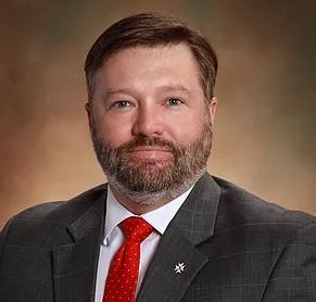 Two people in suits shaking hands over a contract on a wooden table.