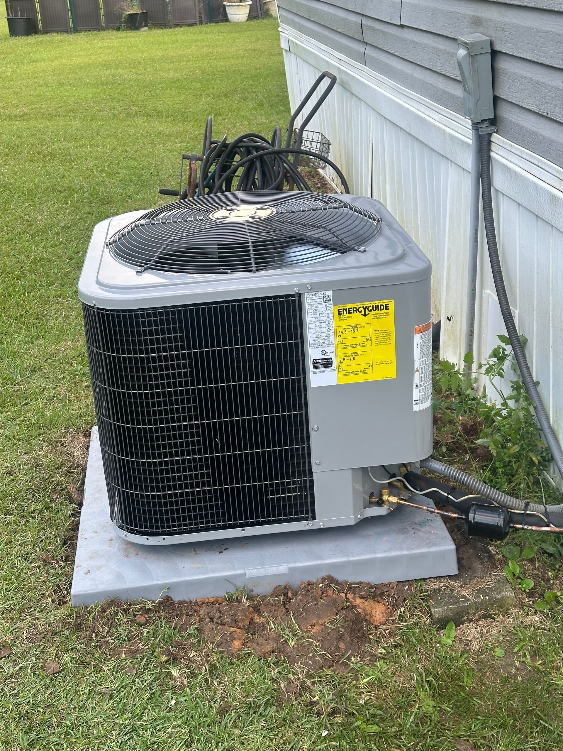 An air conditioner is sitting on top of a concrete base next to a house.