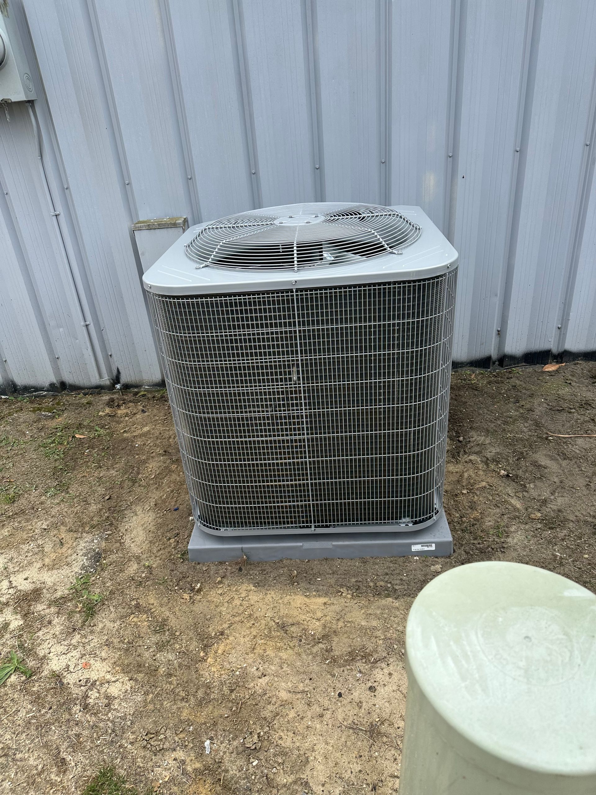 A large air conditioner is sitting in the dirt in front of a building.