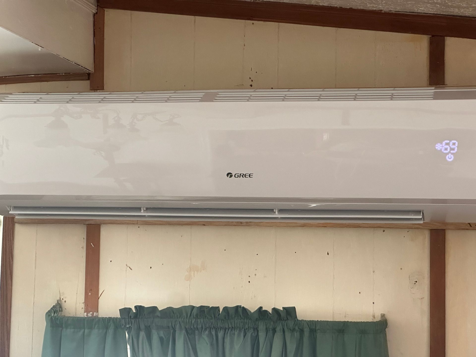 A white air conditioner is hanging from the ceiling in a room with a green curtain.