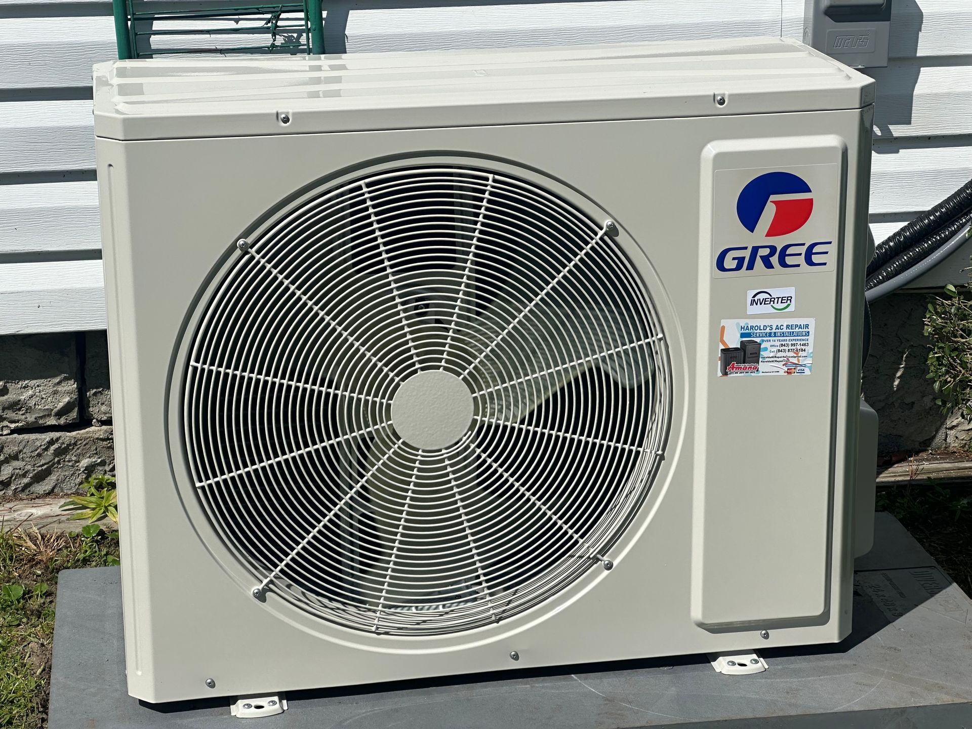 A gree air conditioner is sitting on top of a concrete block.