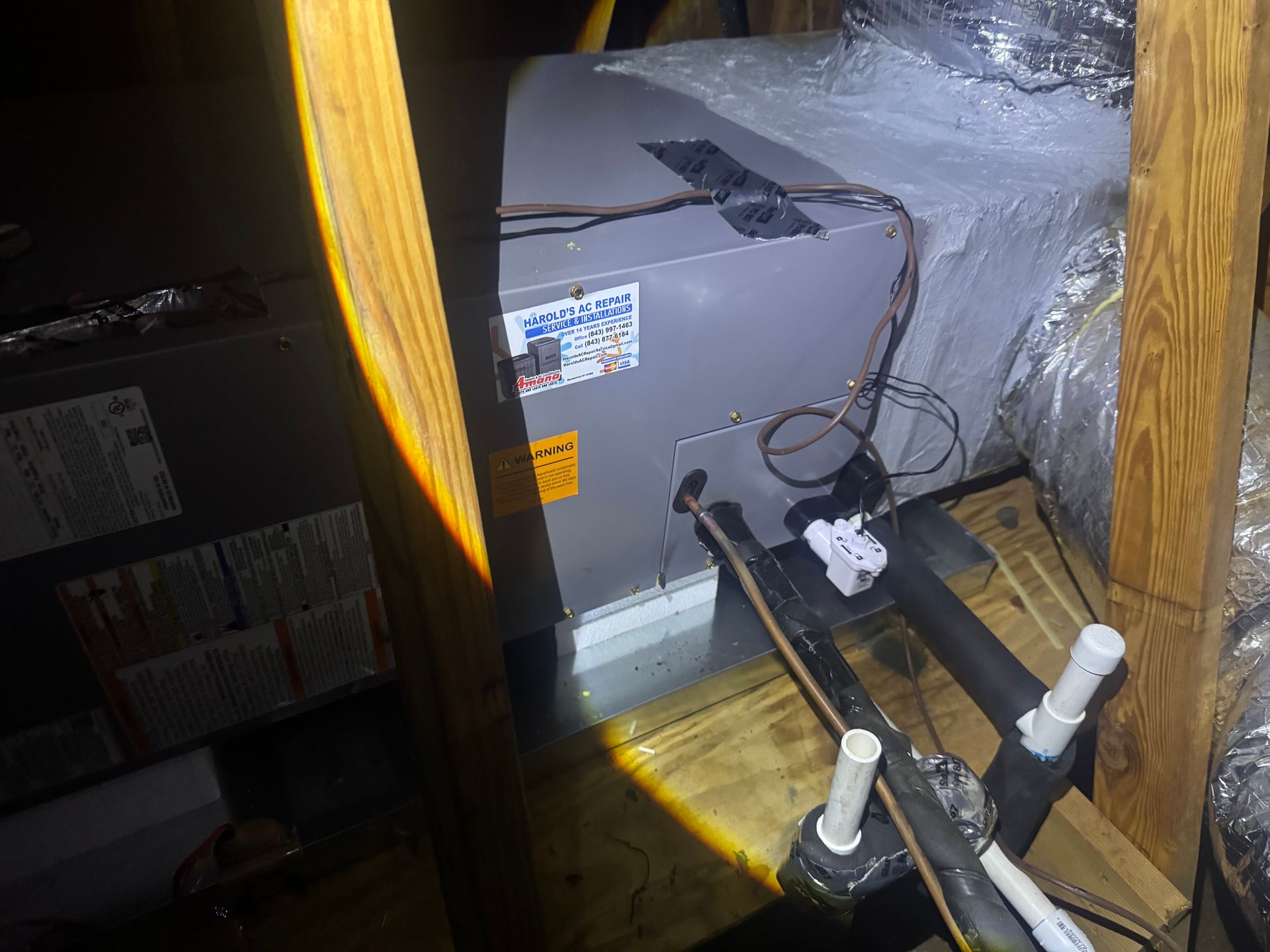 Furnace and exposed HVAC pipes inside a cramped closet with insulation and wooden framing.