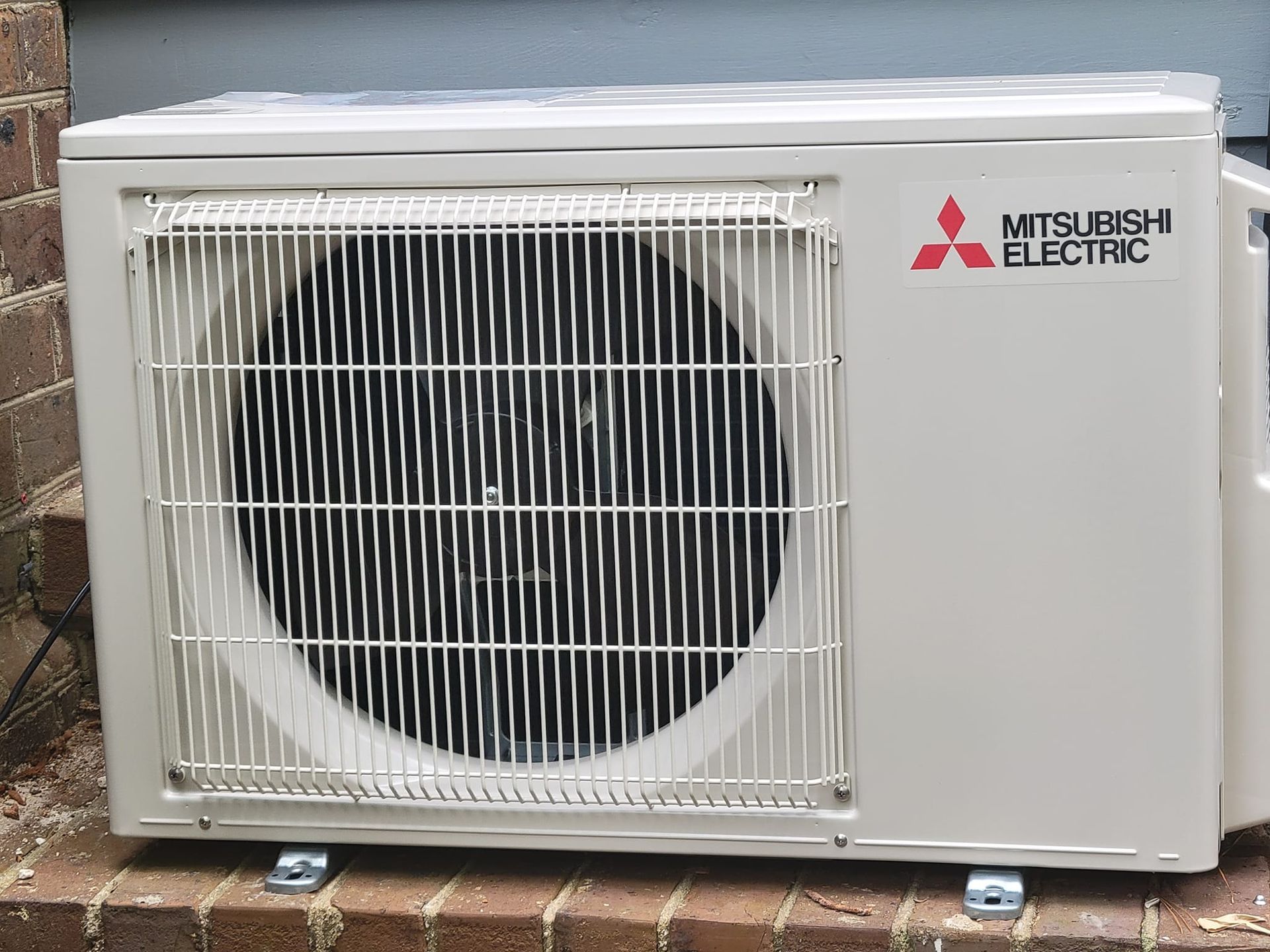 A large air conditioner is sitting in the grass in front of a brick wall