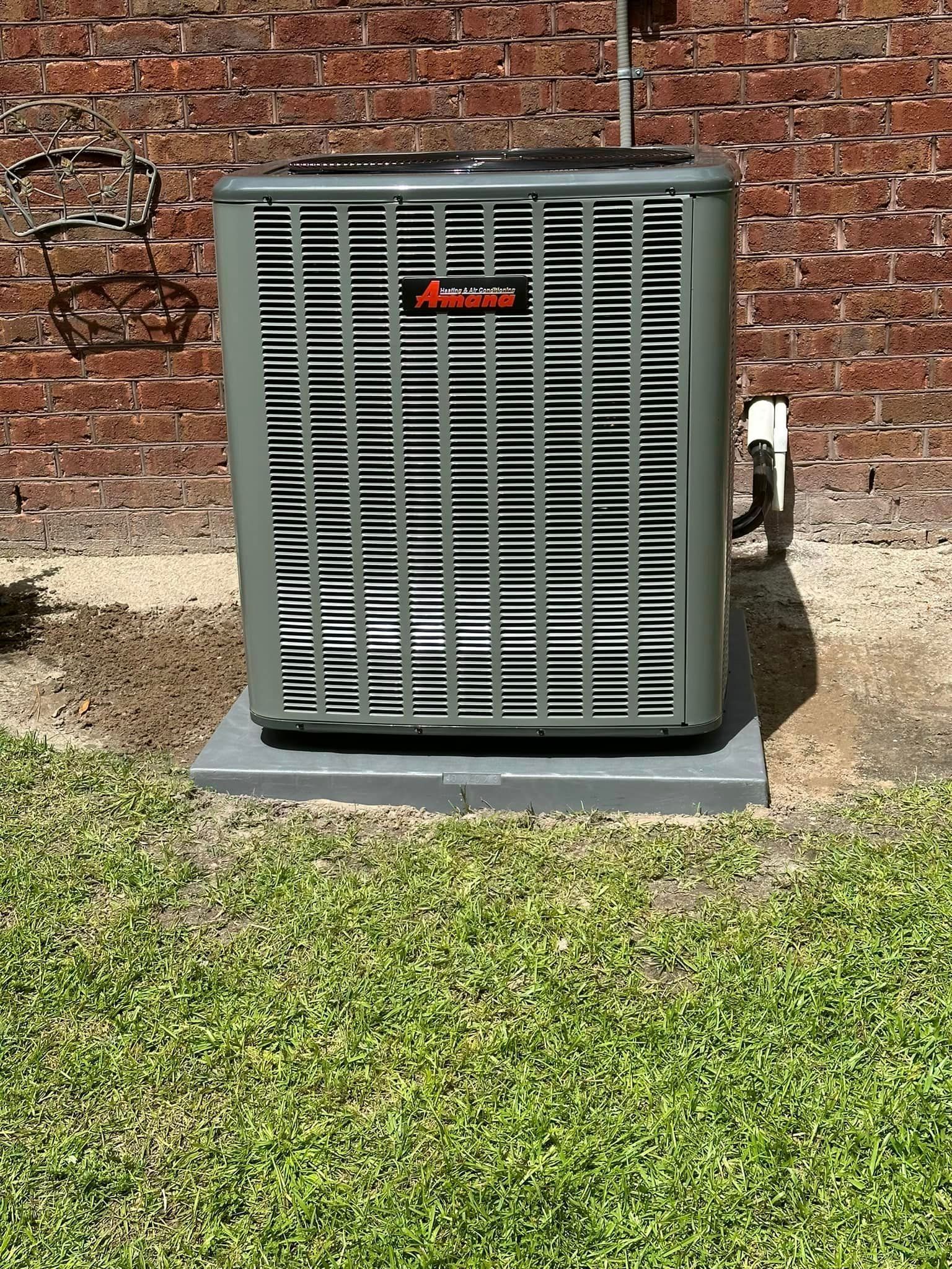 An air conditioner is sitting in the grass in front of a brick building