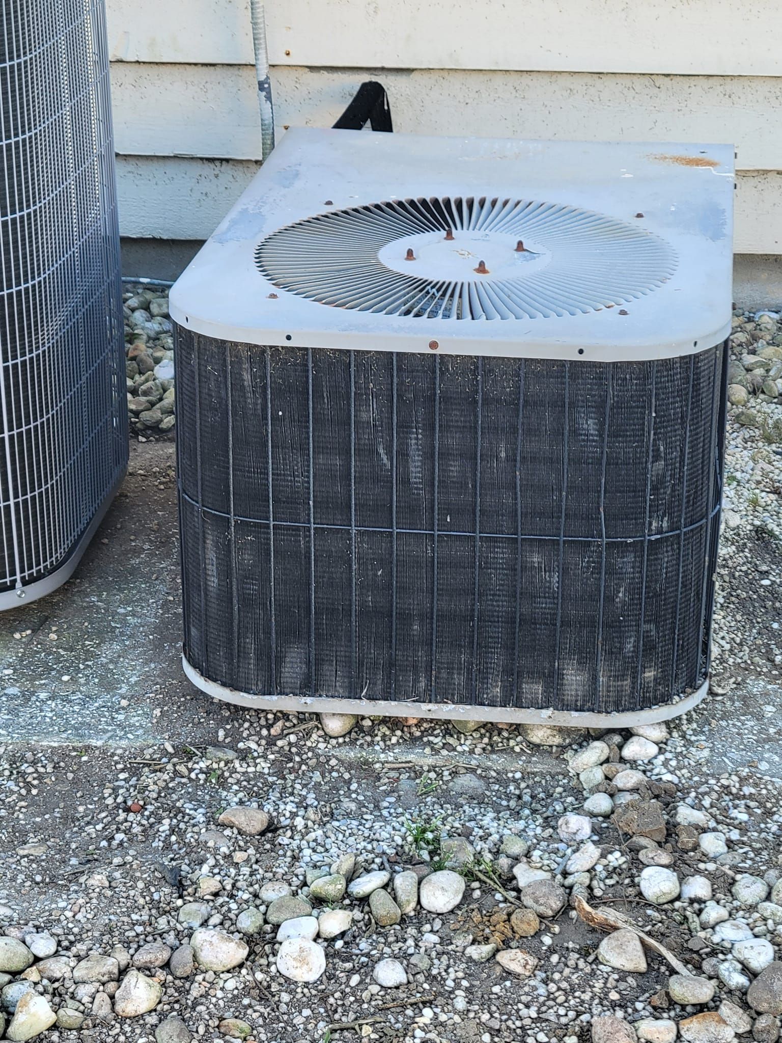 A dirty air conditioner is sitting on the ground next to a house