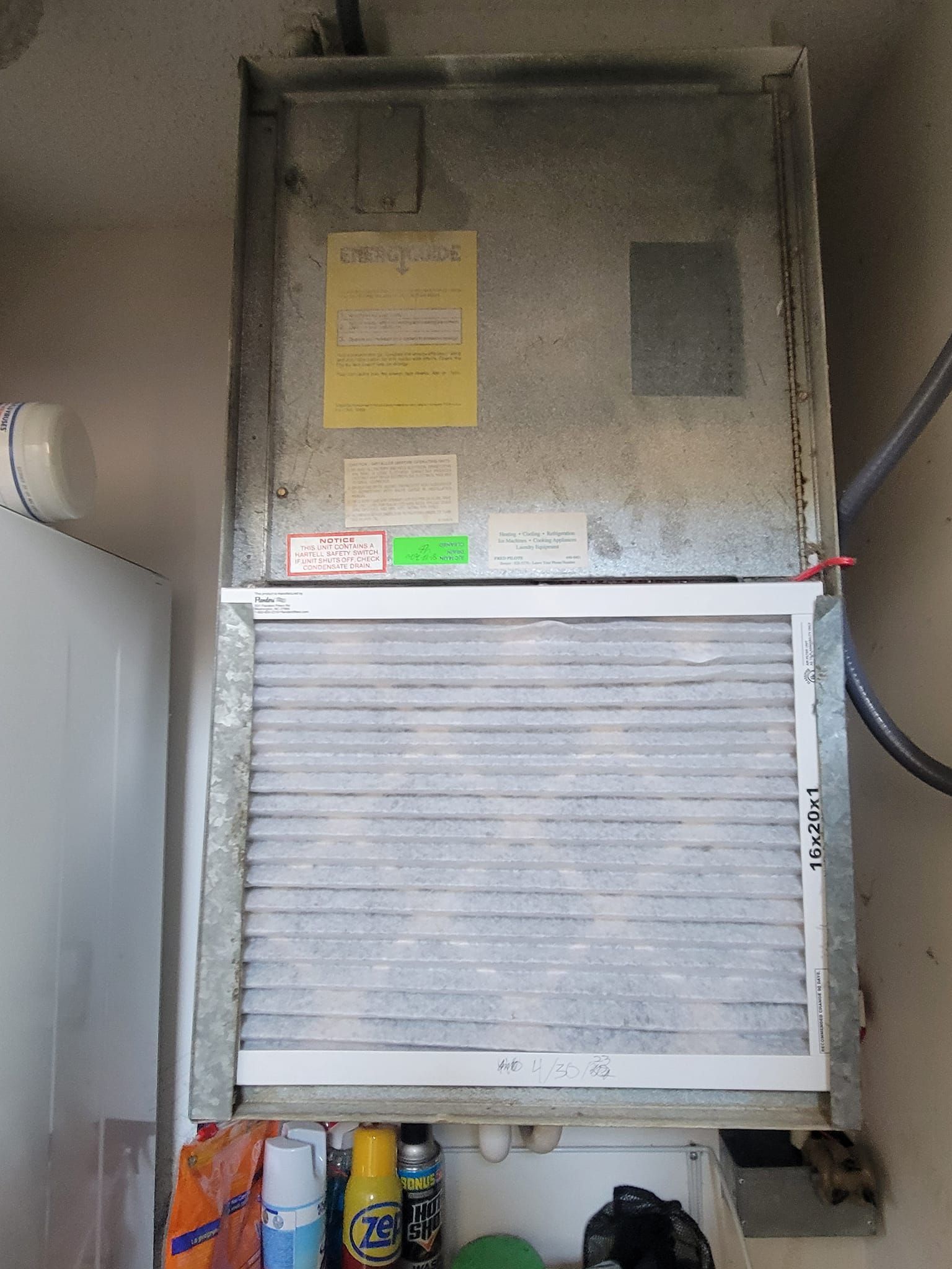 A dirty air conditioner is sitting on a wall next to a refrigerator