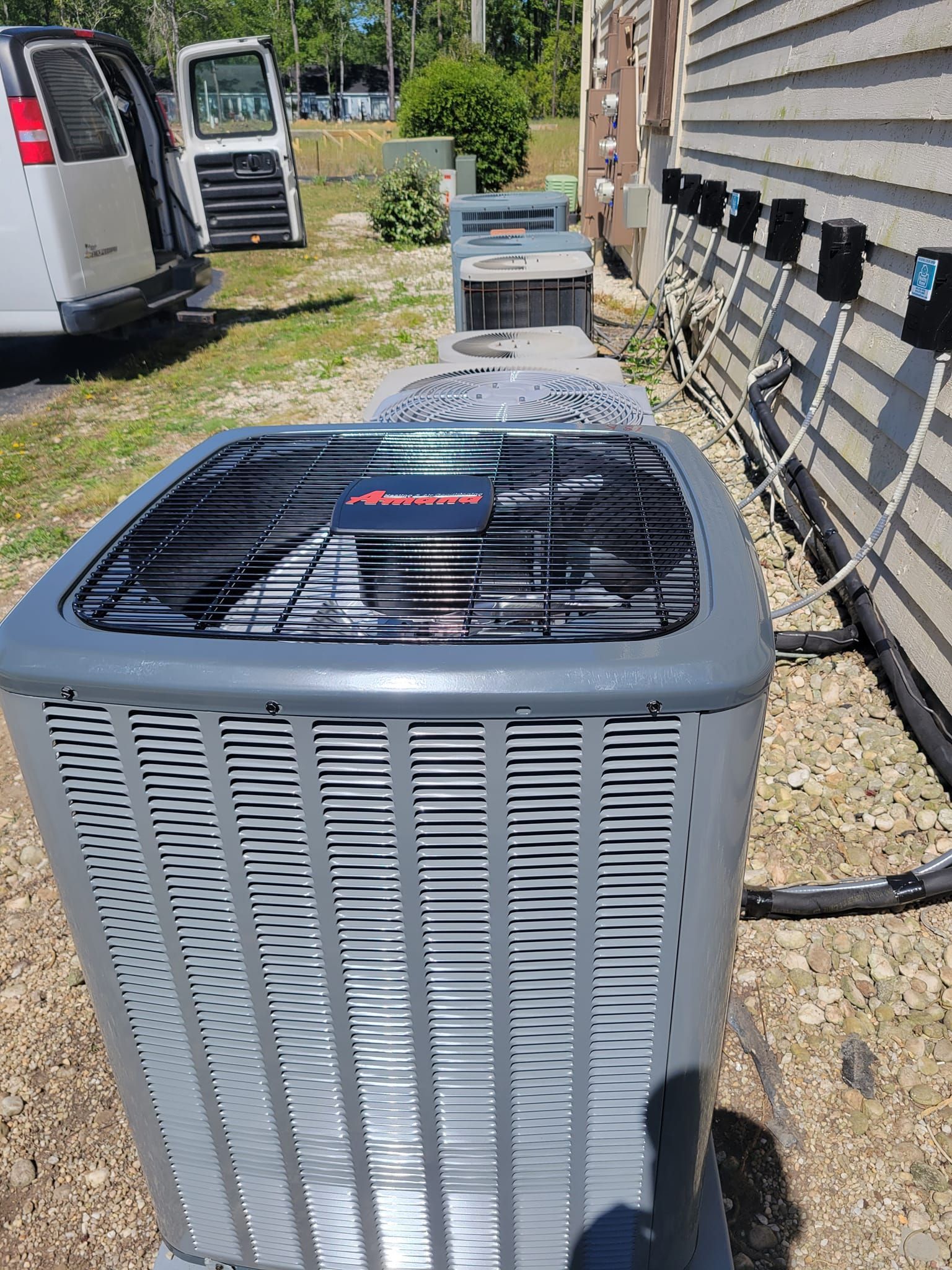 A large air conditioner is sitting outside of a house next to a van