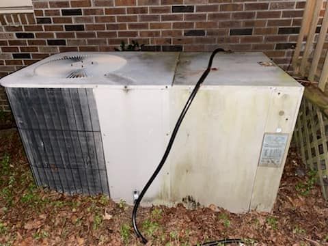 A dirty air conditioner is sitting on the ground 