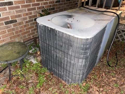 A dirty air conditioner is sitting on the ground next to a brick wall