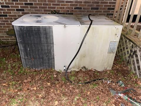 A air conditioner is sitting on the ground next to a brick wall