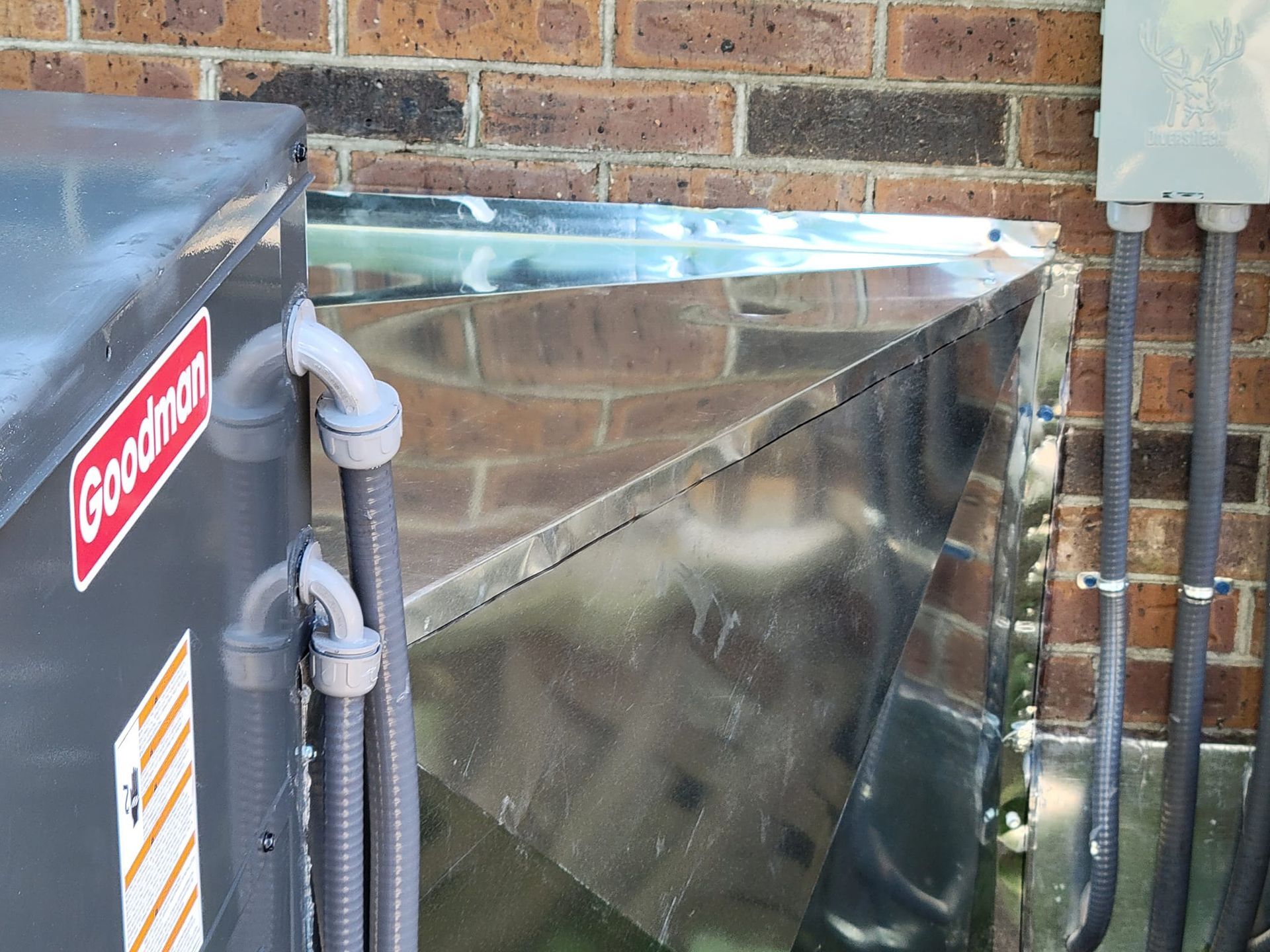 A goodman air conditioner is mounted to a brick wall