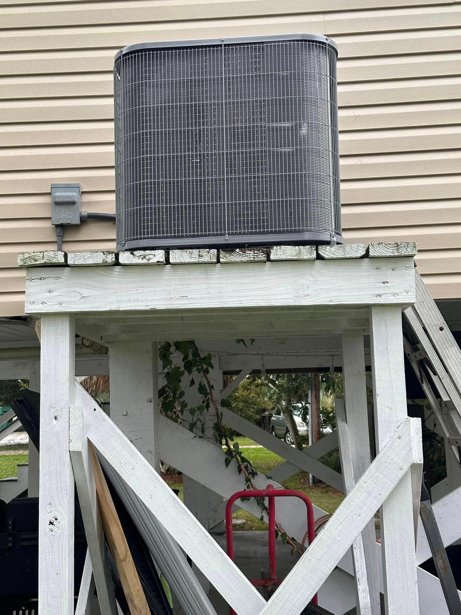 A black air conditioner is sitting on top of a white wooden platform