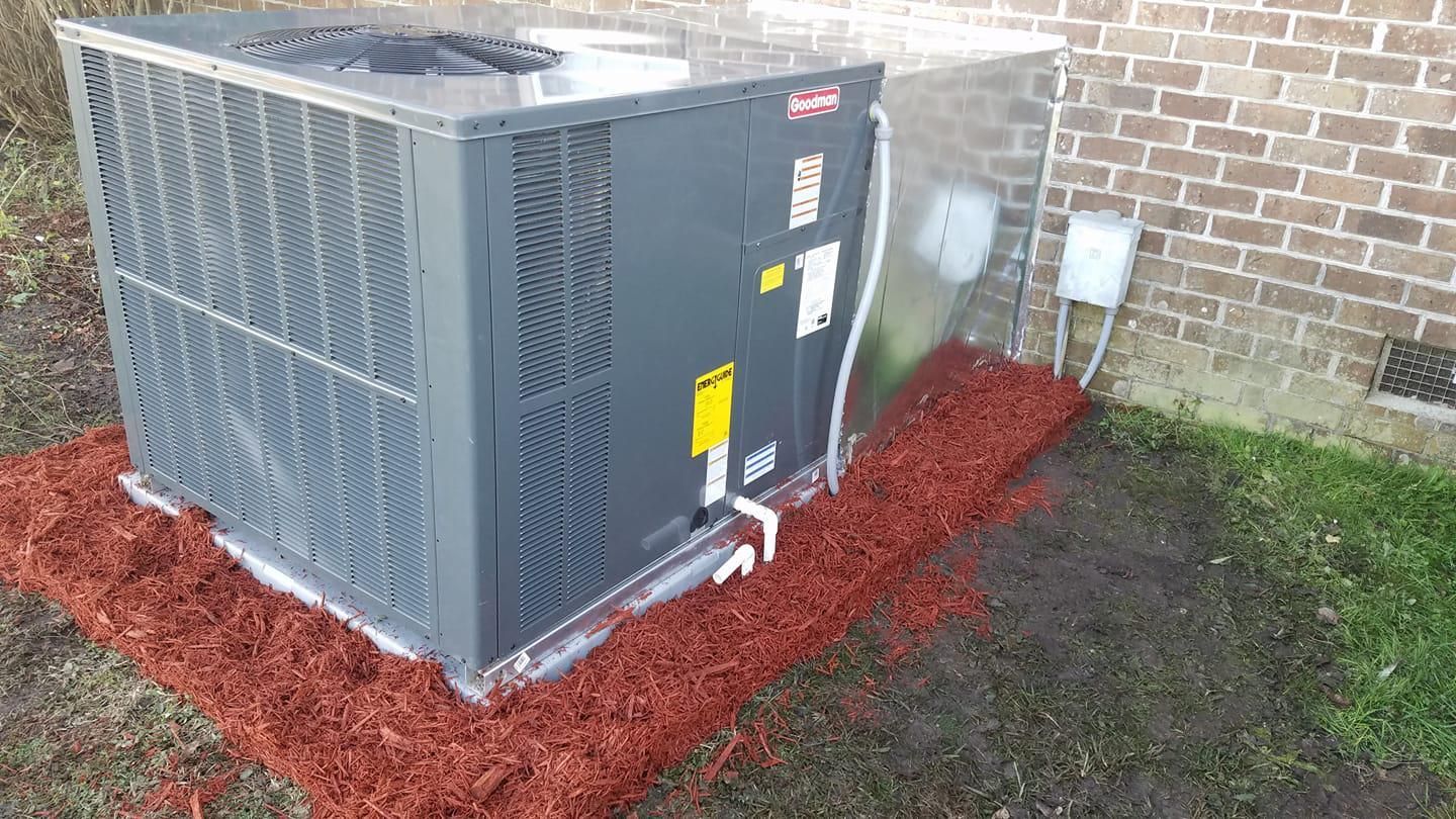 A large air conditioner is sitting on top of a pile of mulch next to a brick building
