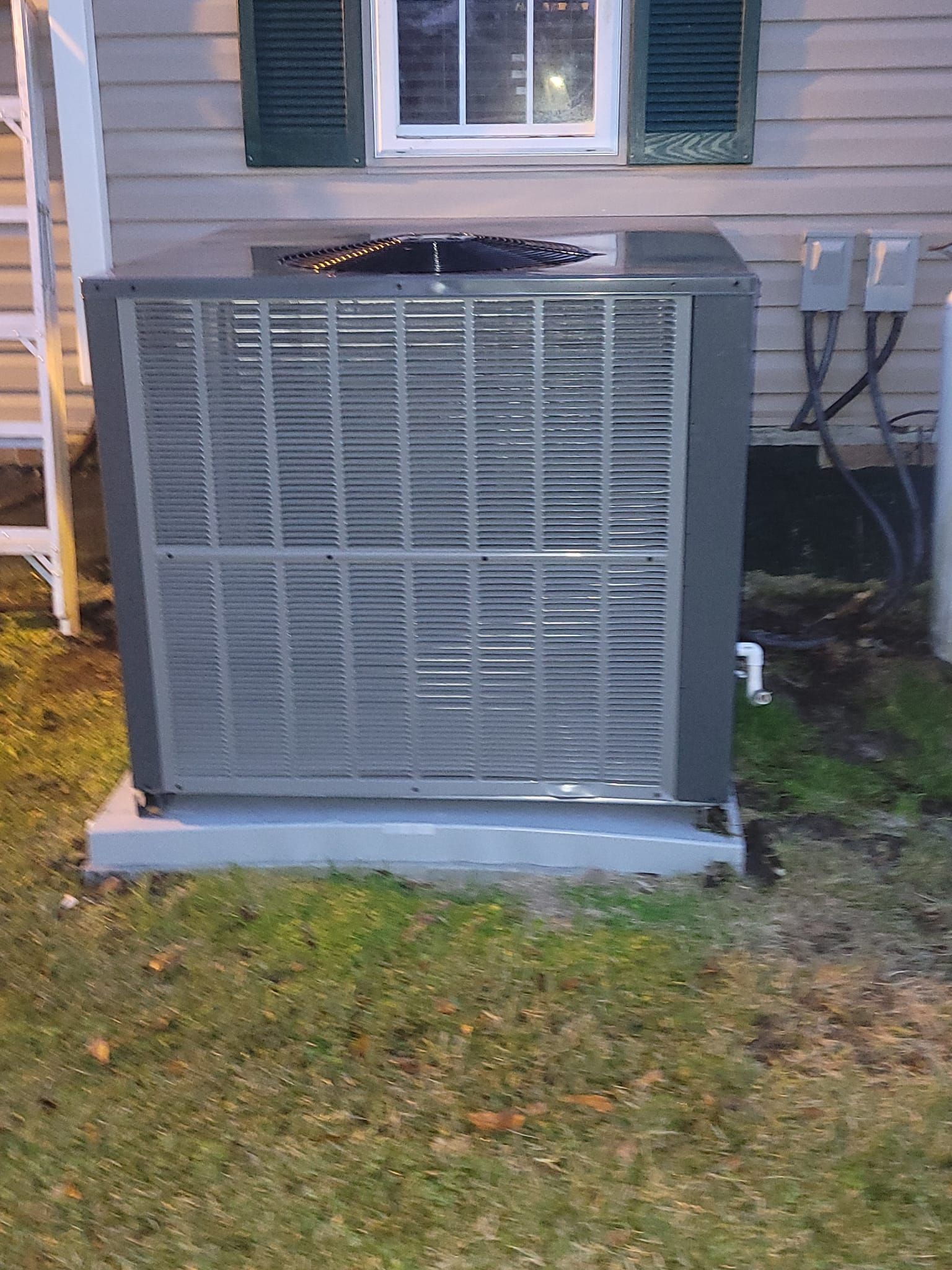 A large air conditioner is sitting in the grass in front of a house