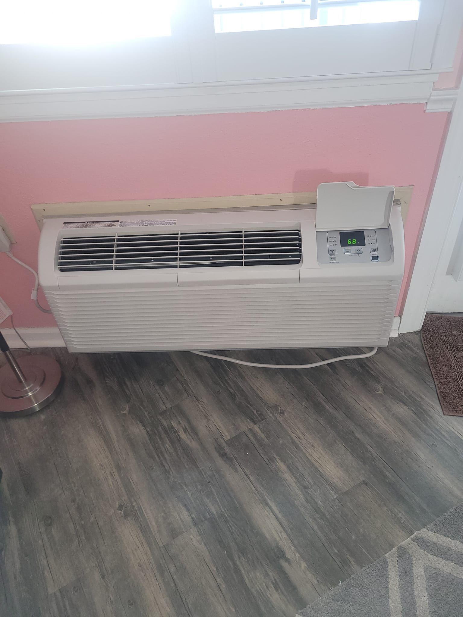 A white air conditioner is sitting on a wooden floor in a room next to a window