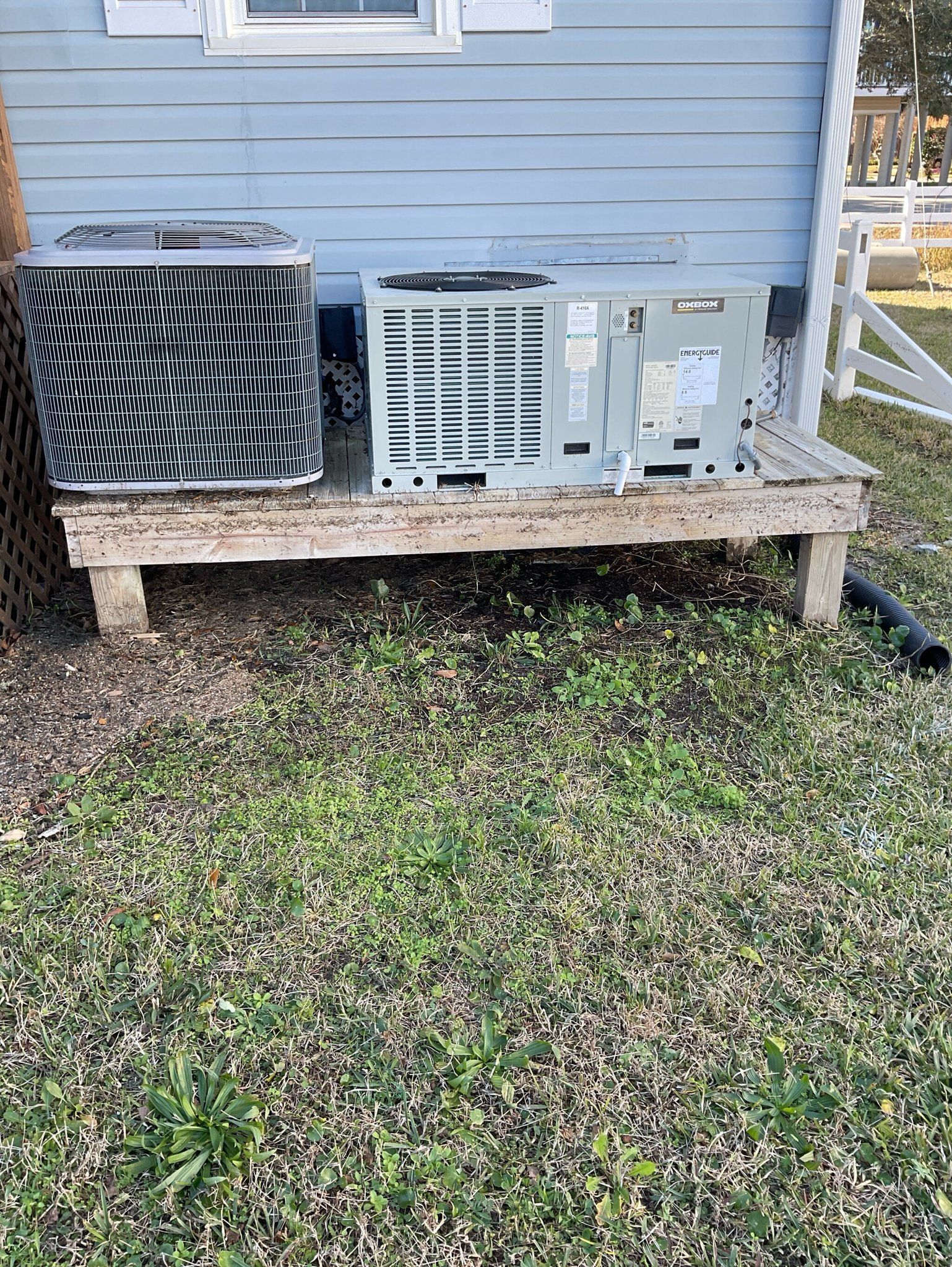 Two air conditioners are sitting on a wooden platform in front of a house
