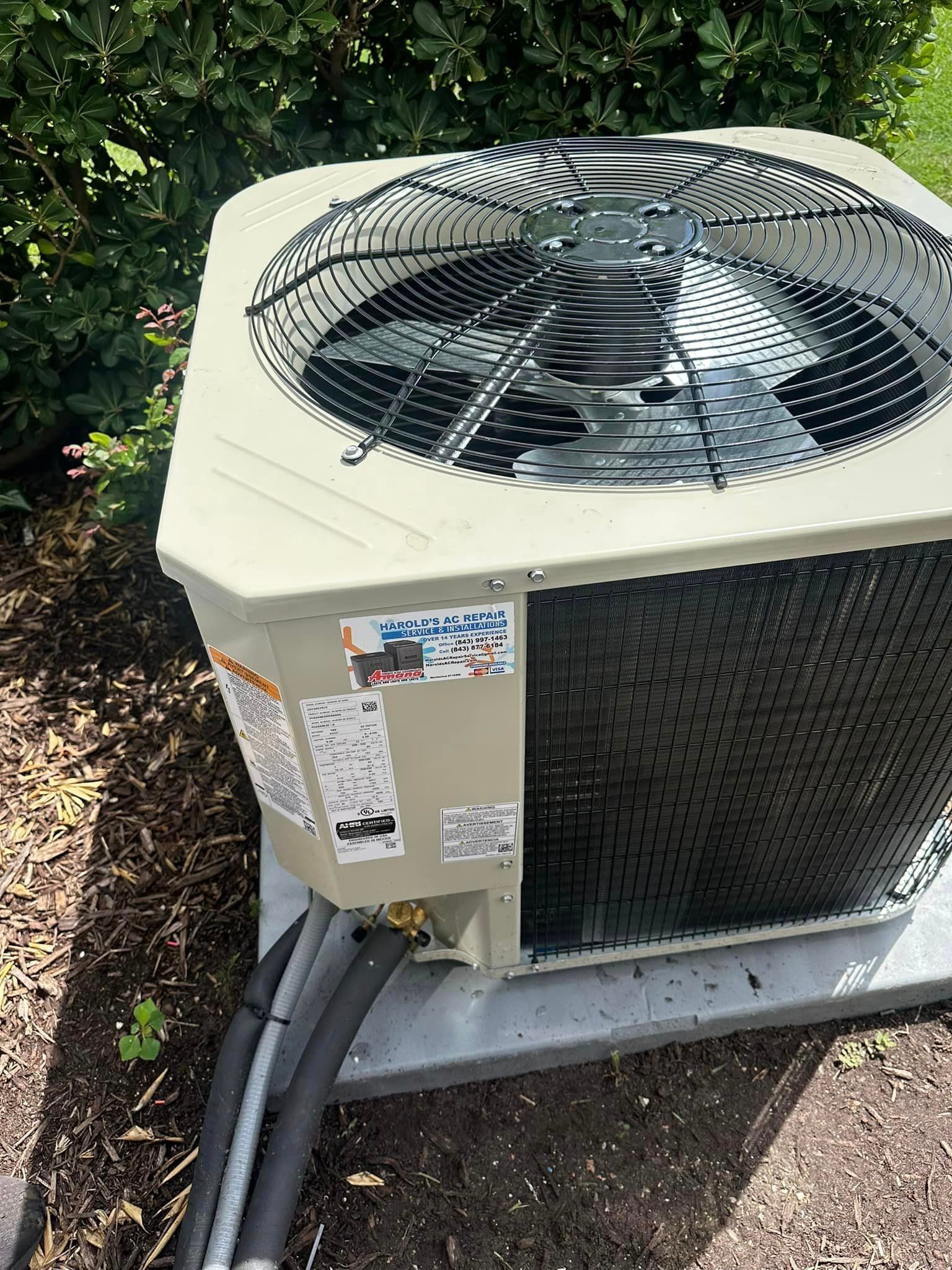 A large air conditioner is sitting on the ground next to a bush