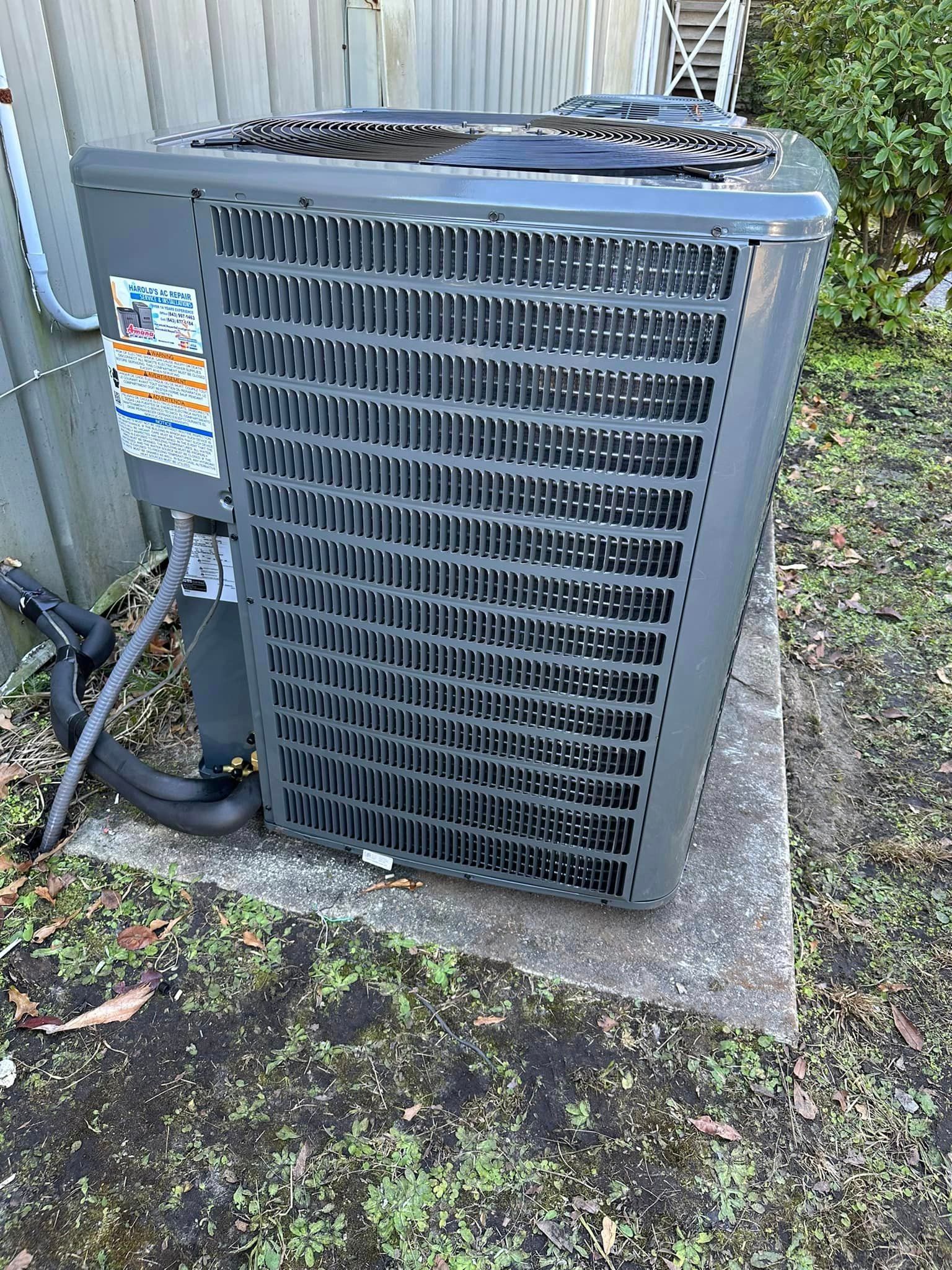 A gray air conditioner is sitting on a concrete platform in front of a brick building