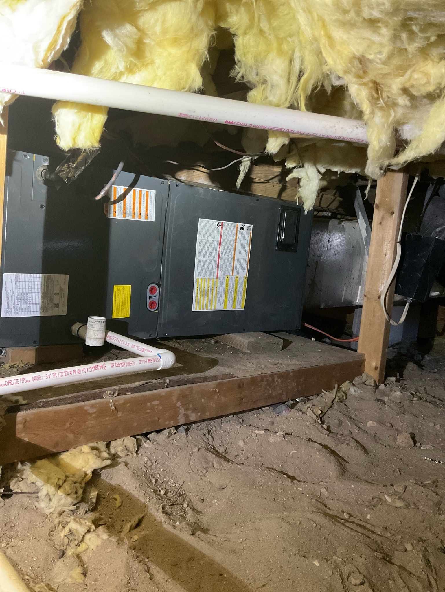 An air conditioner is sitting under a ceiling in an attic
