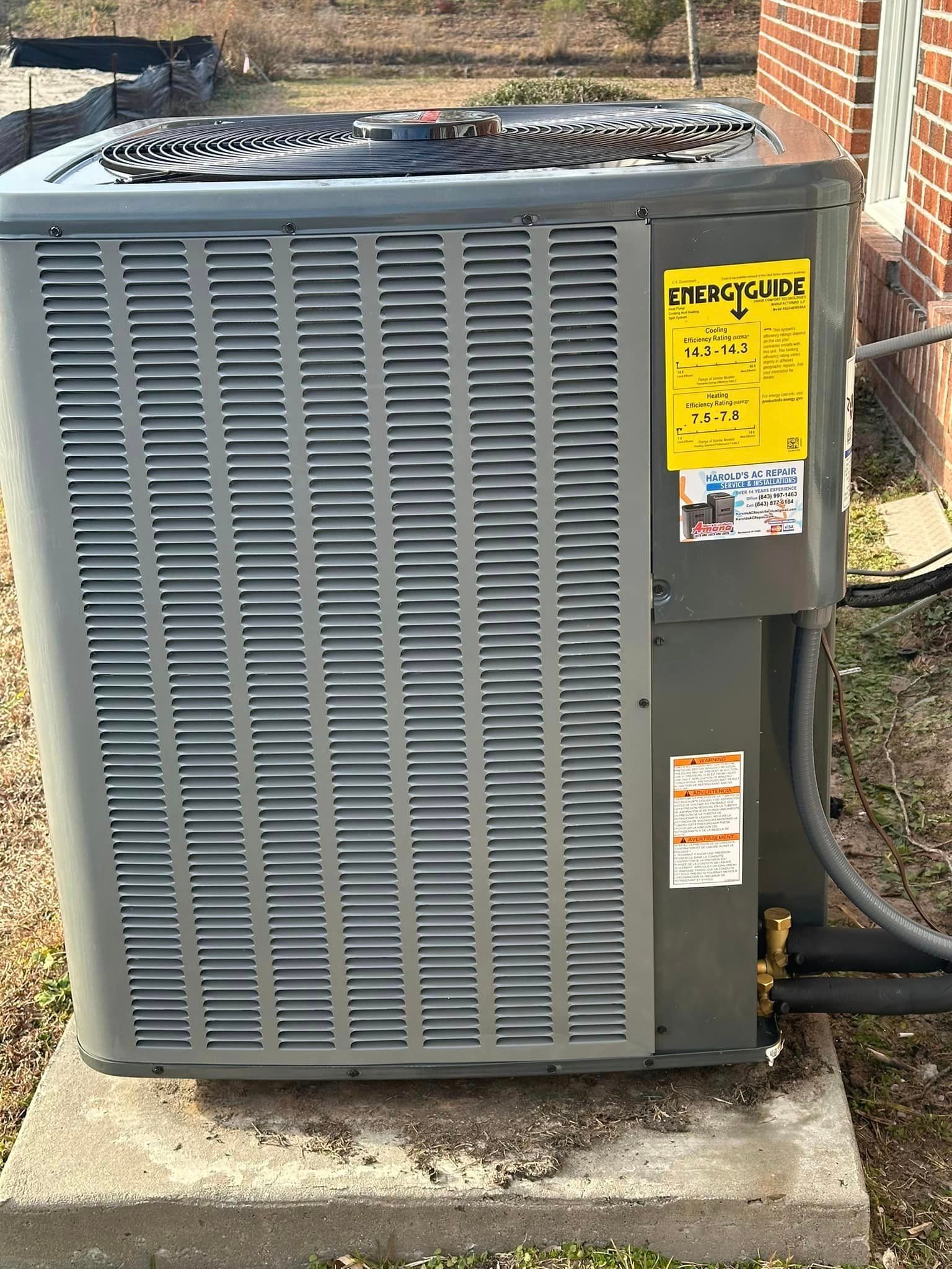 A large air conditioner is sitting on top of a concrete block in front of a brick building.