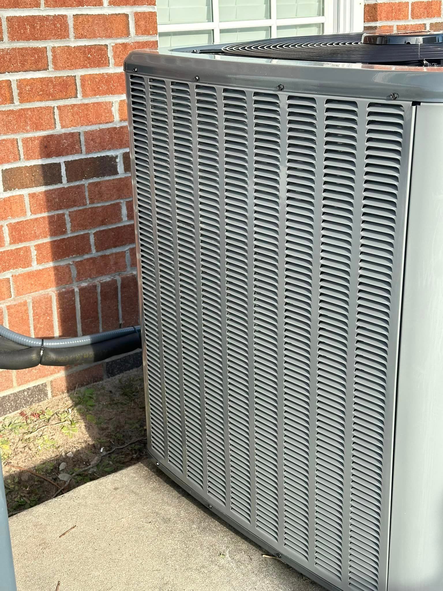 A large air conditioner is sitting outside of a brick building.