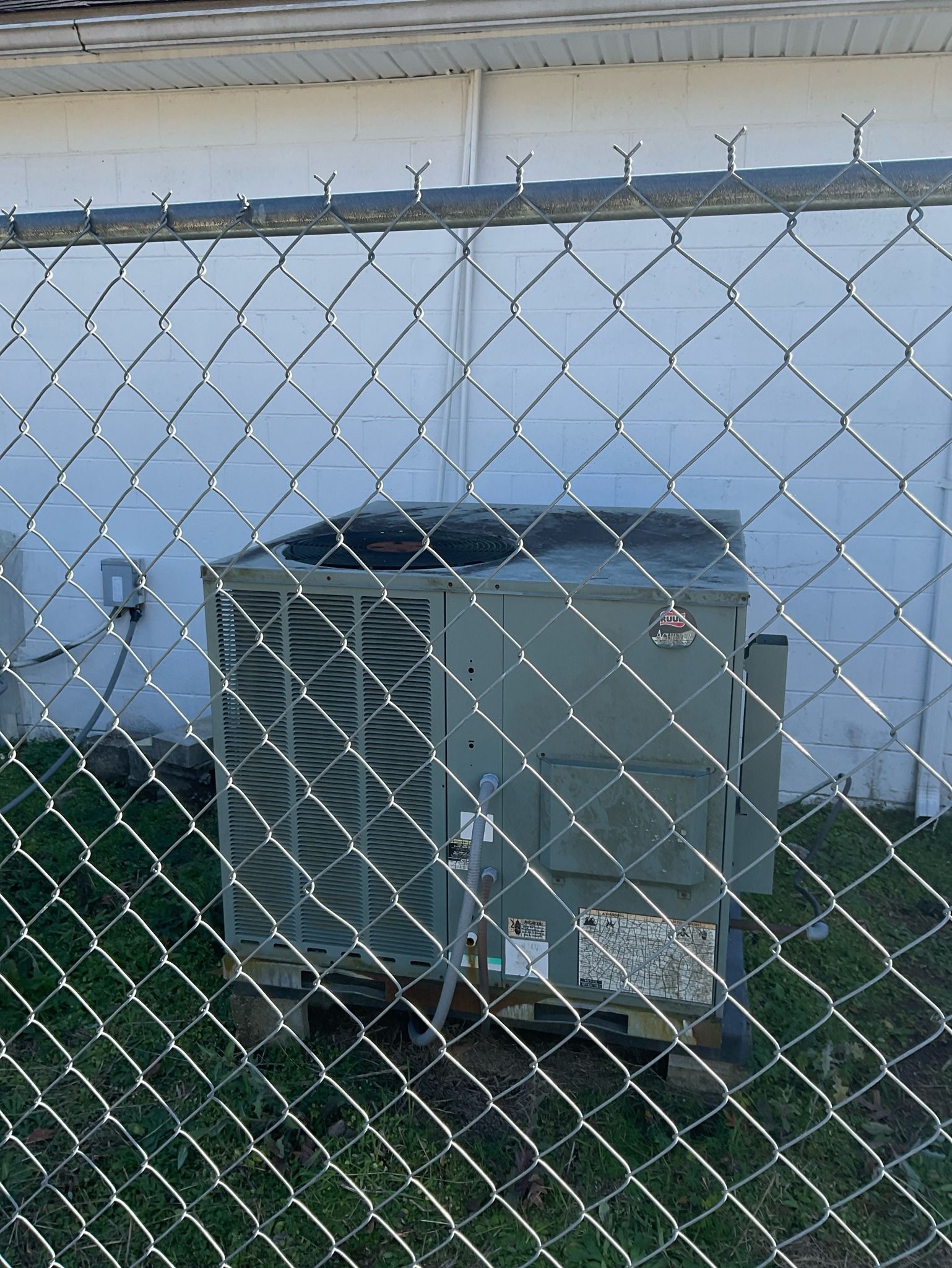 An air conditioner is behind a chain link fence