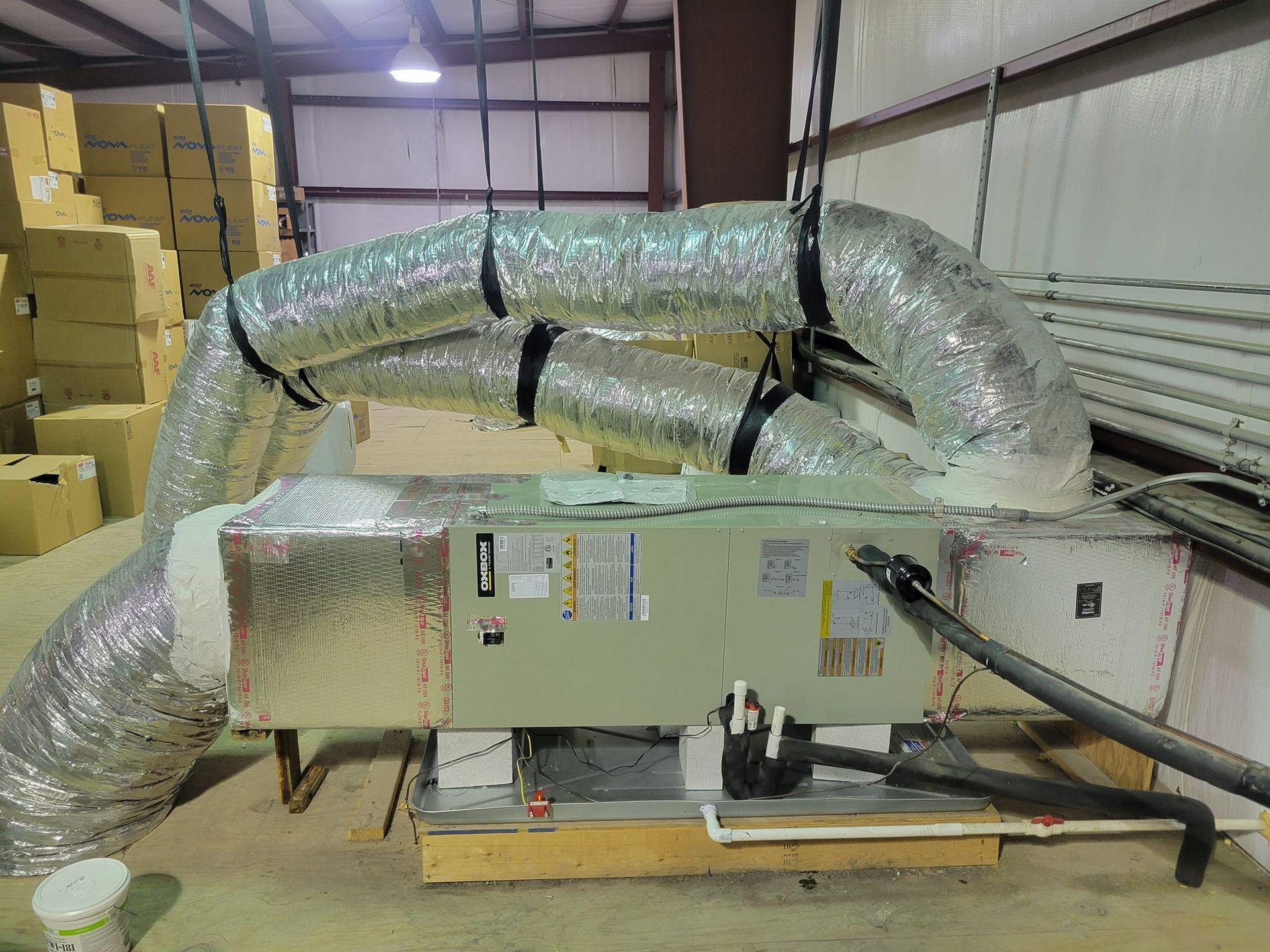 A large air conditioner is sitting in a warehouse with a bunch of ducts coming out of it.