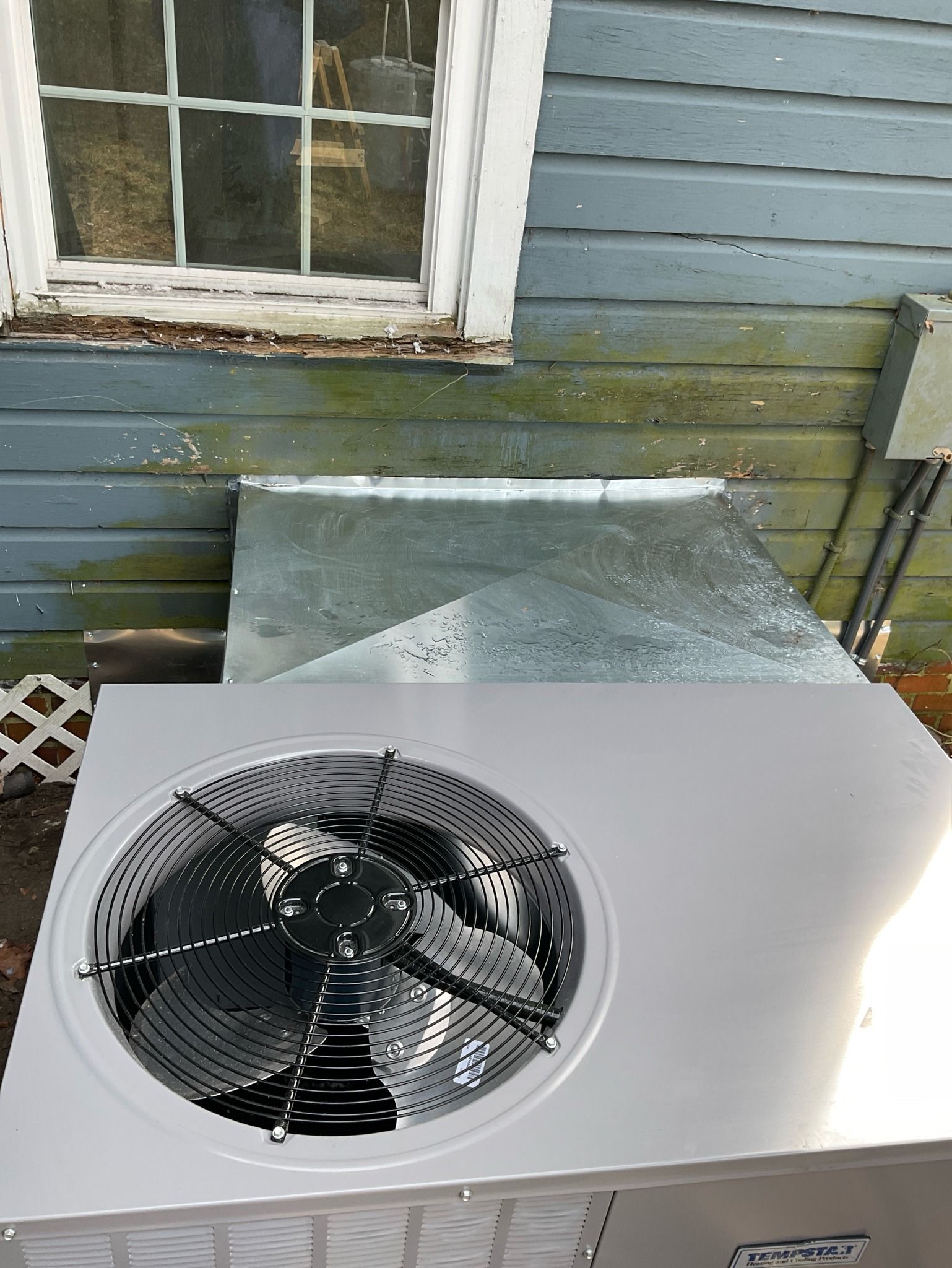 A fan is sitting on the side of a building next to a window