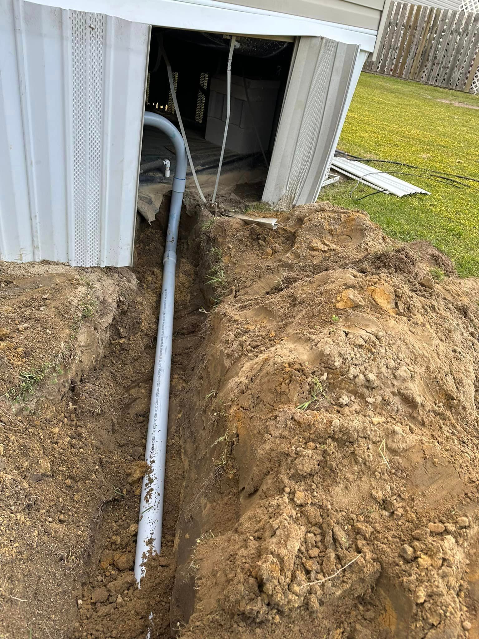 A pipe is being installed in the dirt next to a house