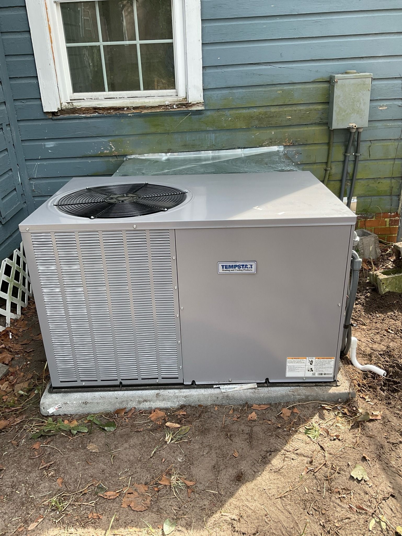 An air conditioner is sitting outside of a house next to a window