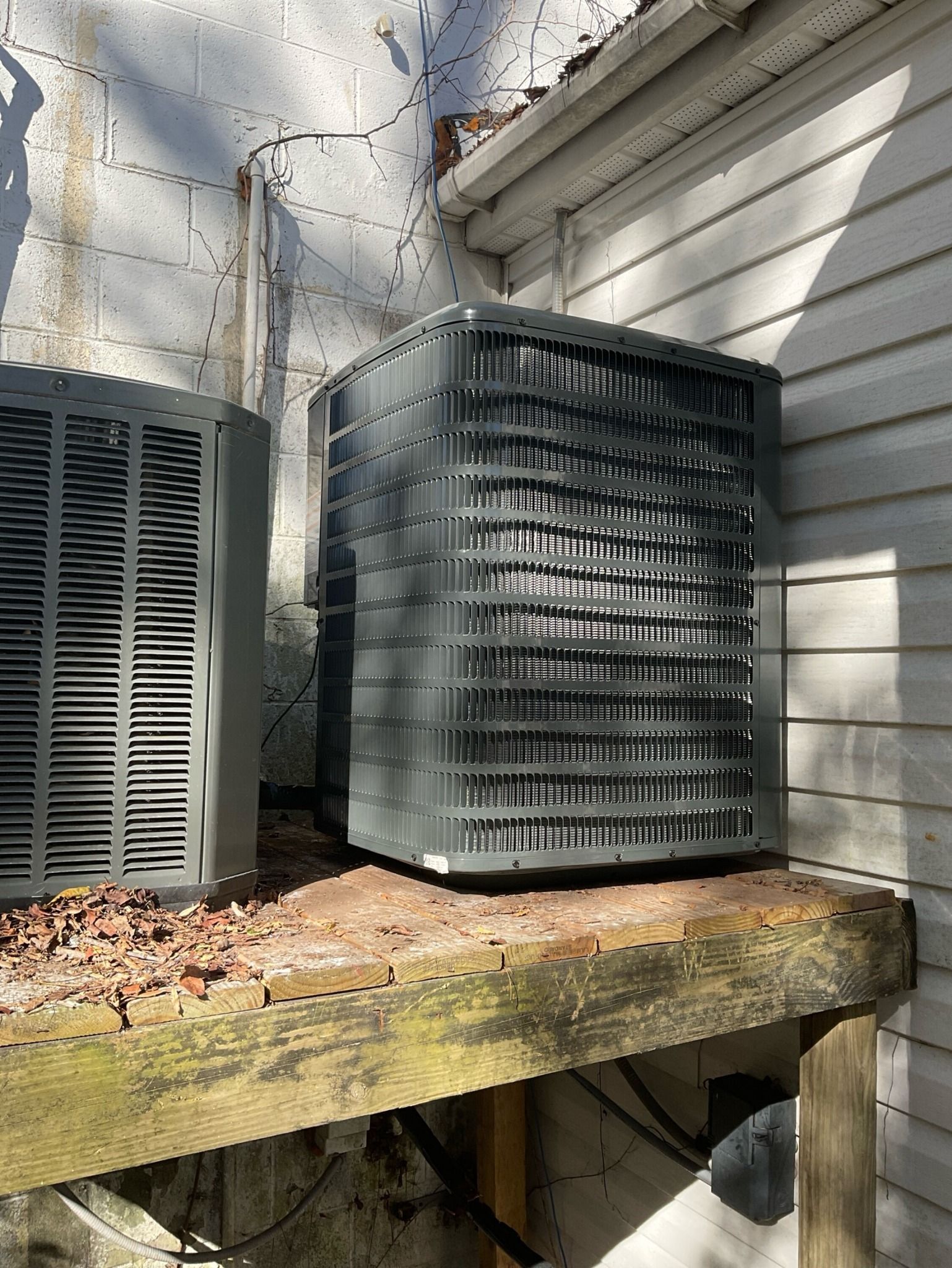 Two air conditioners are sitting on a wooden shelf outside of a house