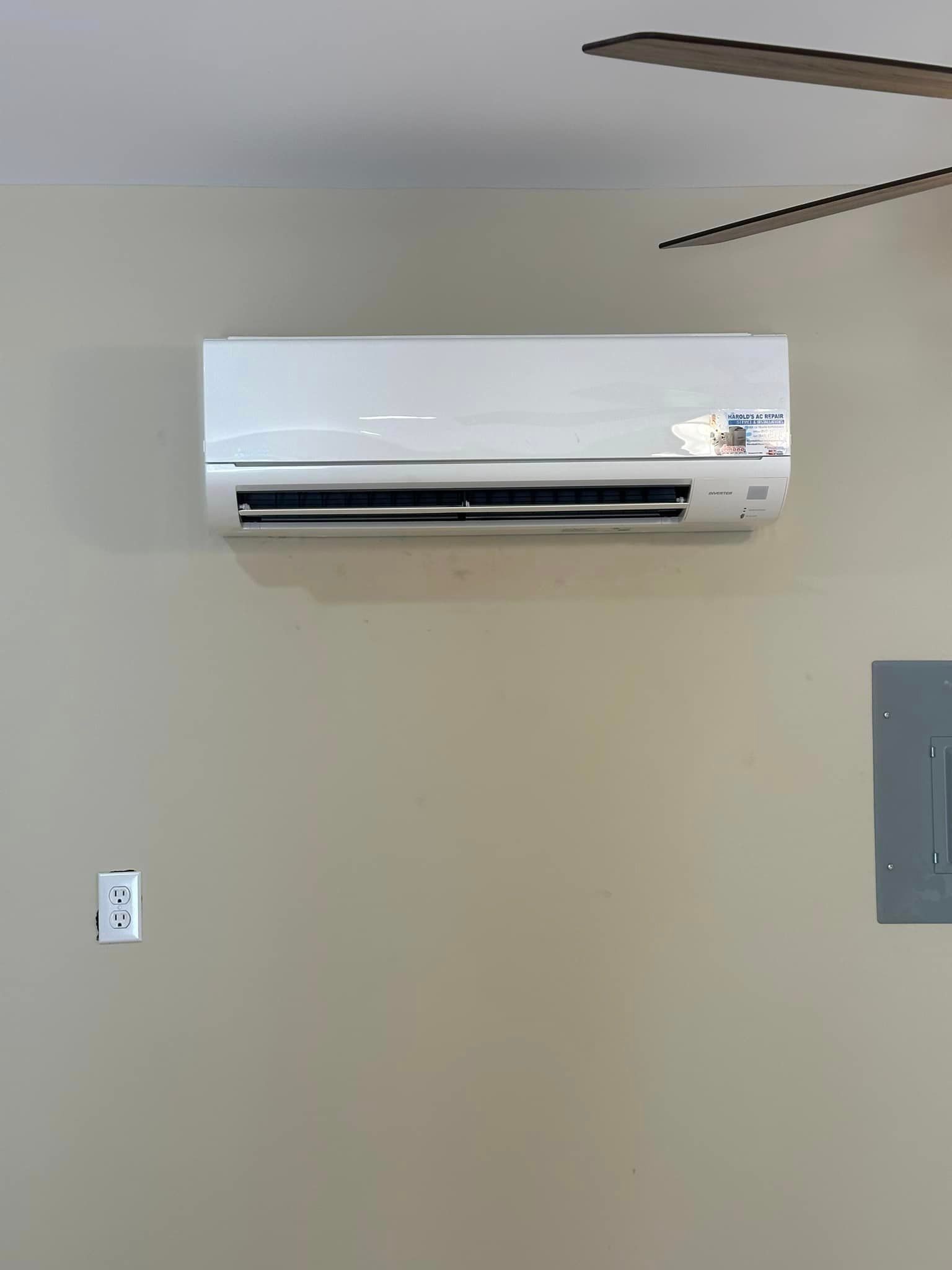 A white air conditioner is hanging on a wall next to a ceiling fan