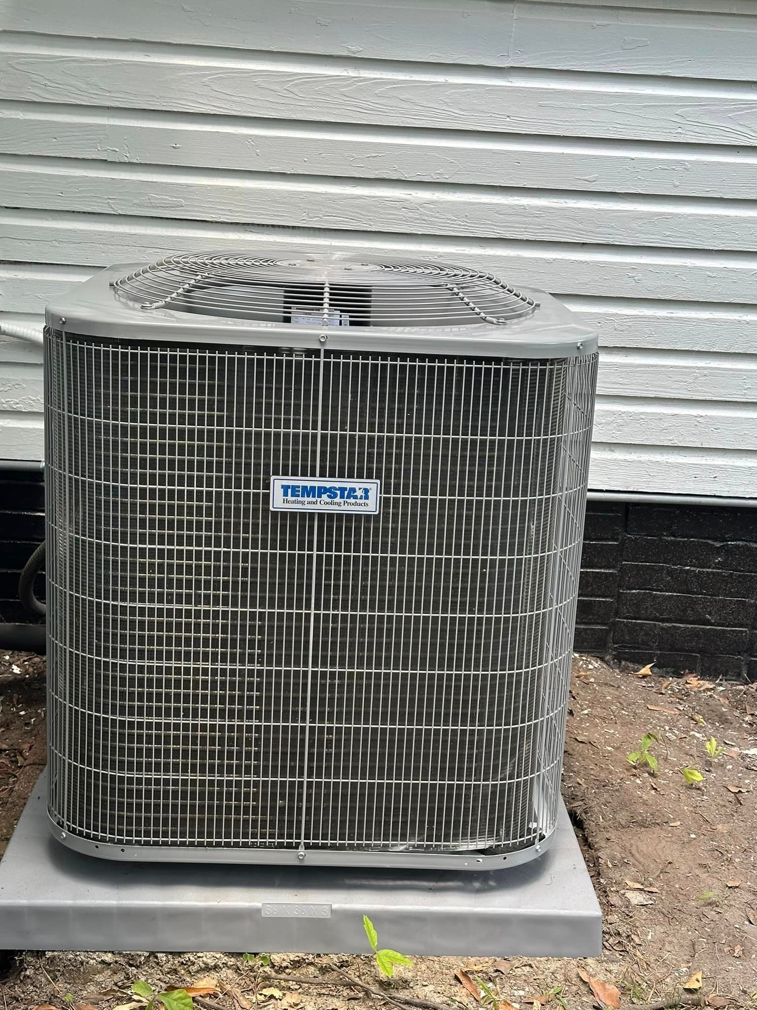 A black air conditioner is sitting outside of a house.