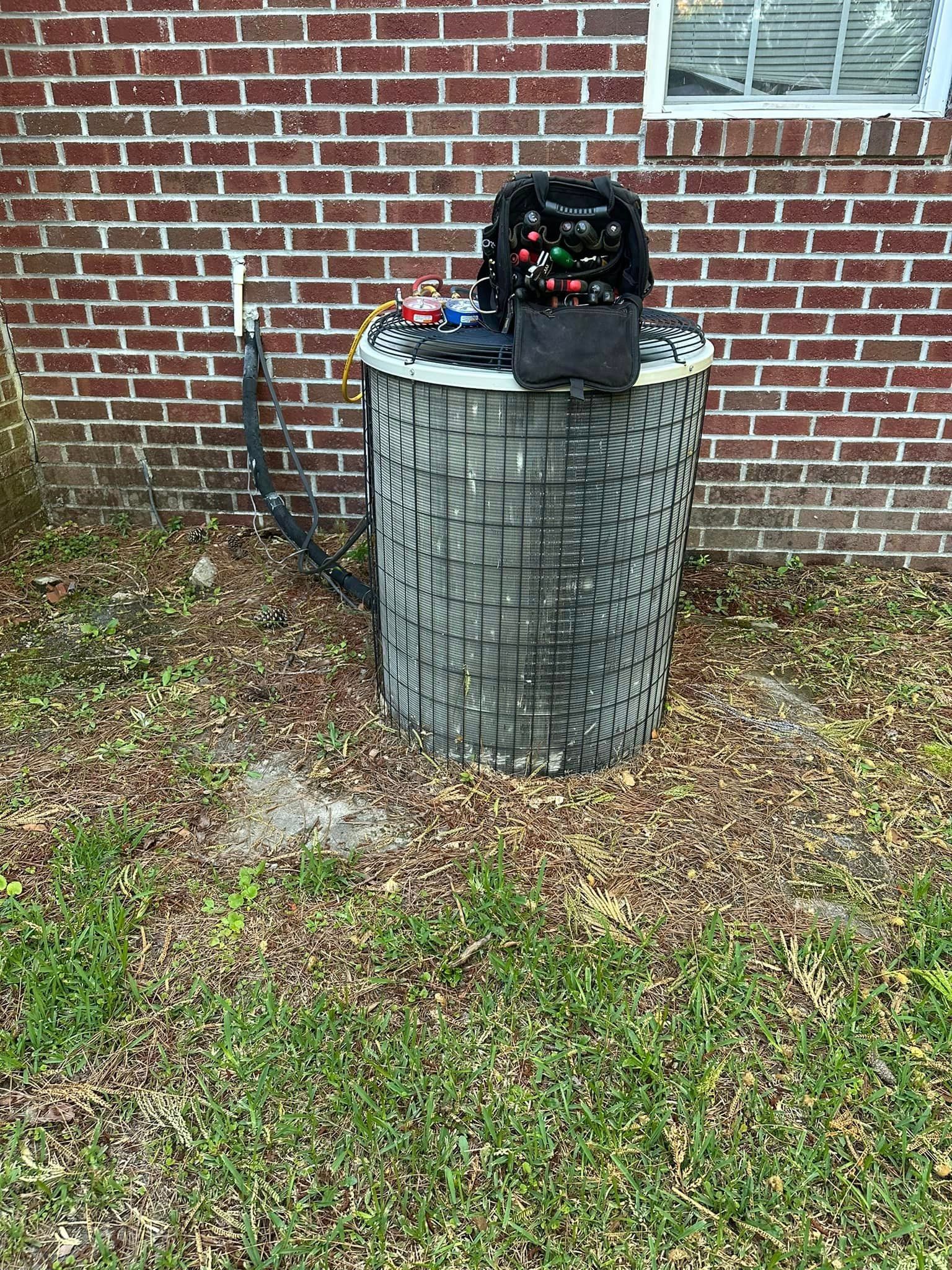 An air conditioner is sitting in the grass in front of a brick building