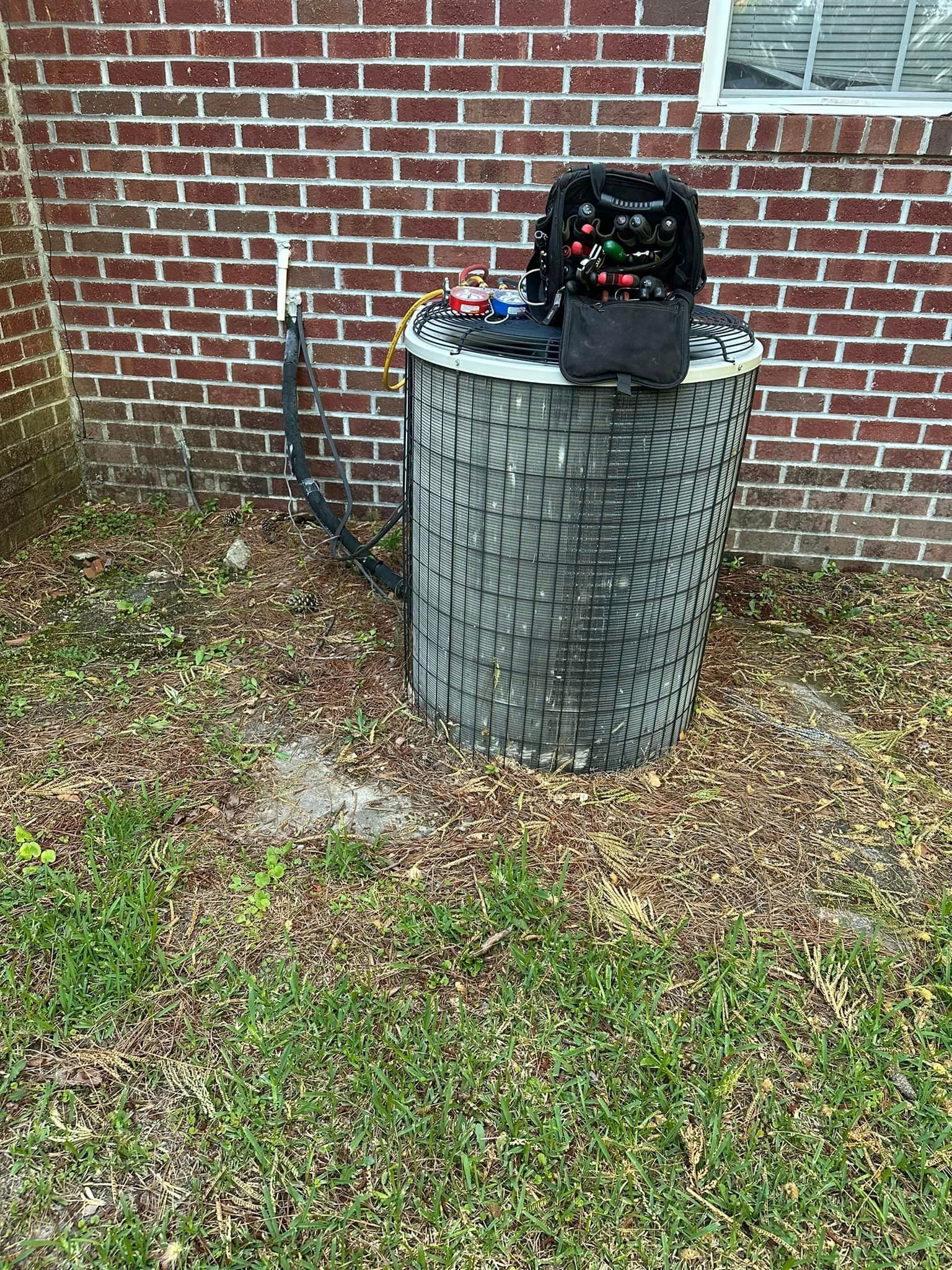 An air conditioner is sitting in the grass in front of a brick building