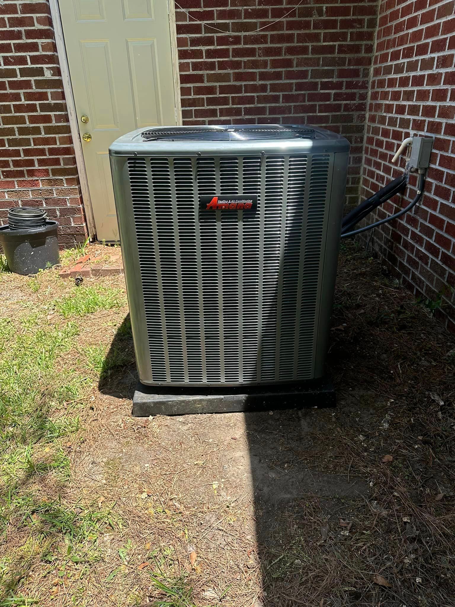 A large air conditioner is sitting outside of a brick building.