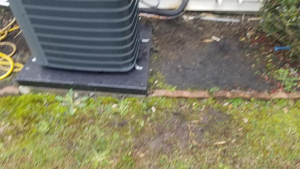 A black air conditioner is sitting in the grass next to a hose