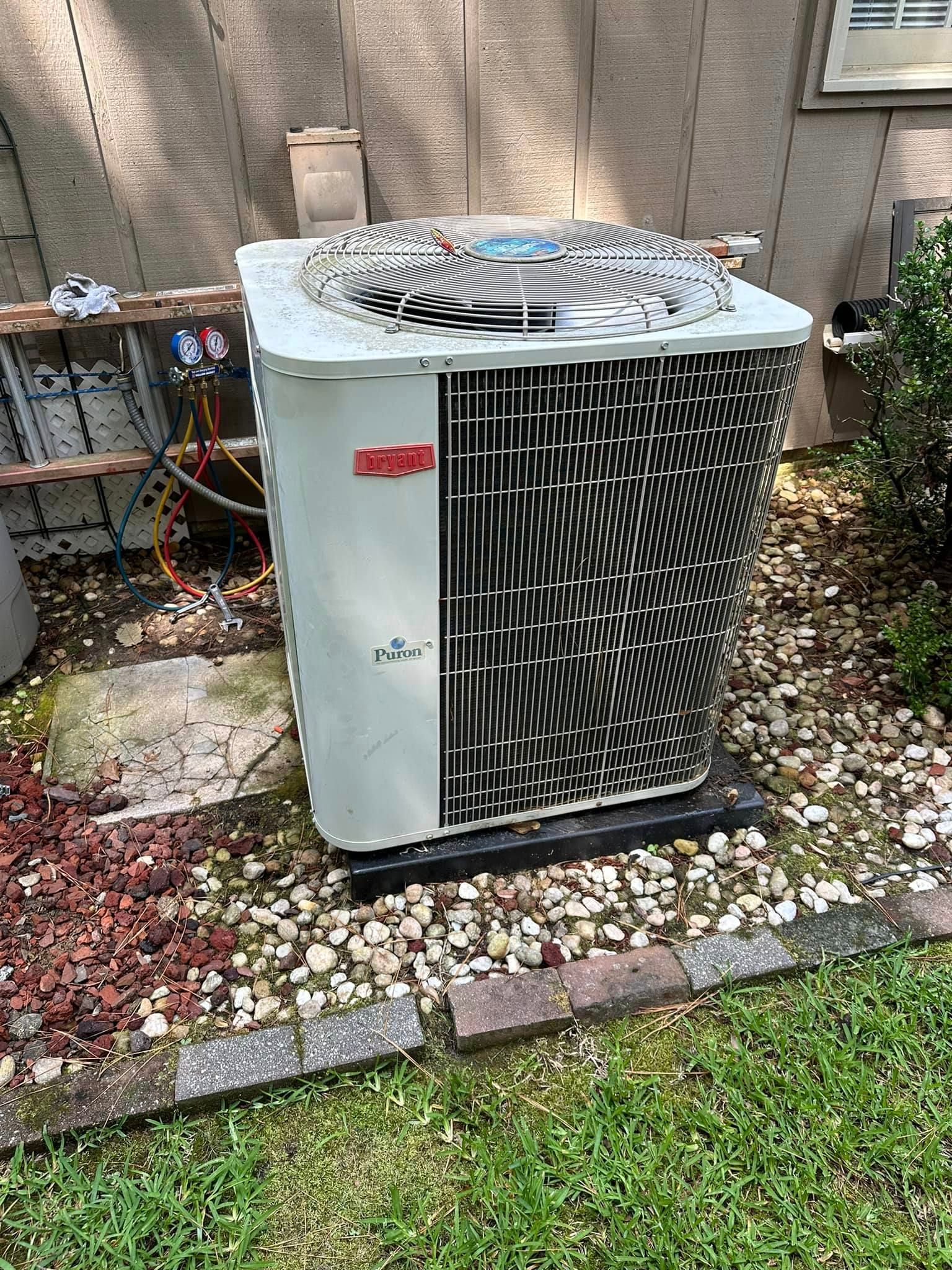 A white air conditioner is sitting in the grass in front of a house