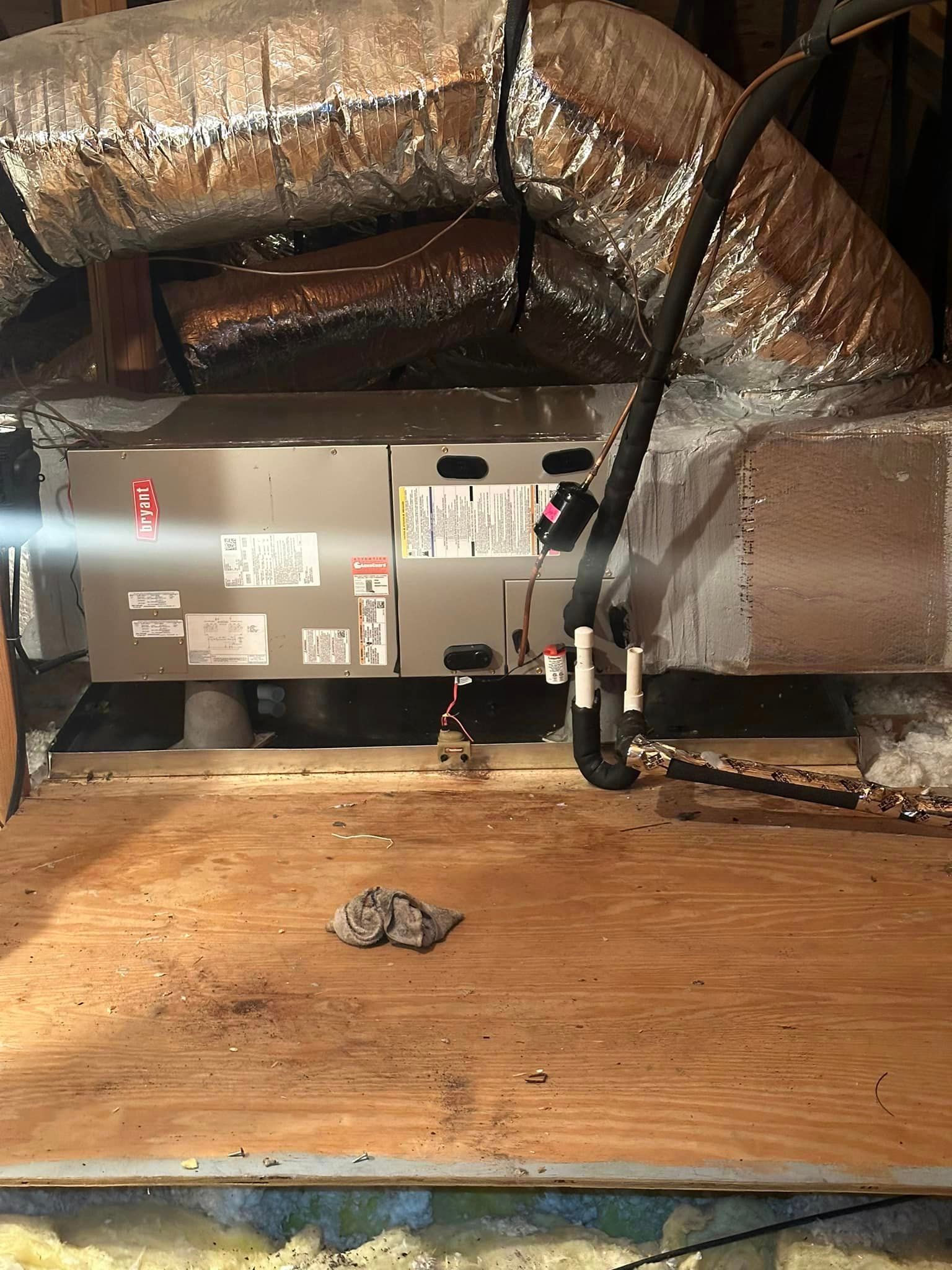 An air conditioner is sitting on top of a wooden floor in an attic
