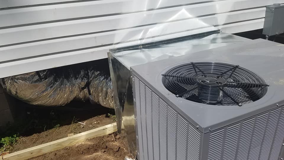 A large air conditioner is sitting under a building next to a duct