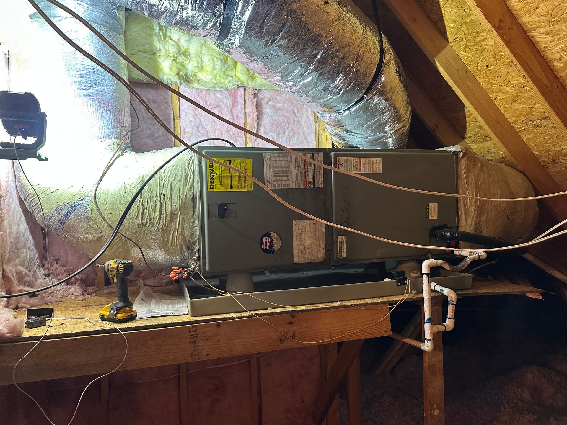 An air conditioner is sitting on top of a wooden table in an attic.