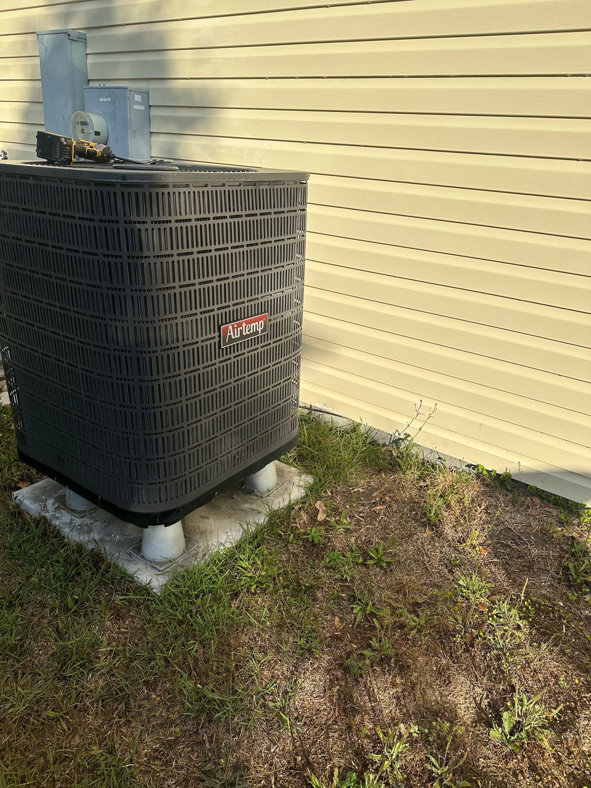 A black air conditioner is sitting in the grass next to a house.