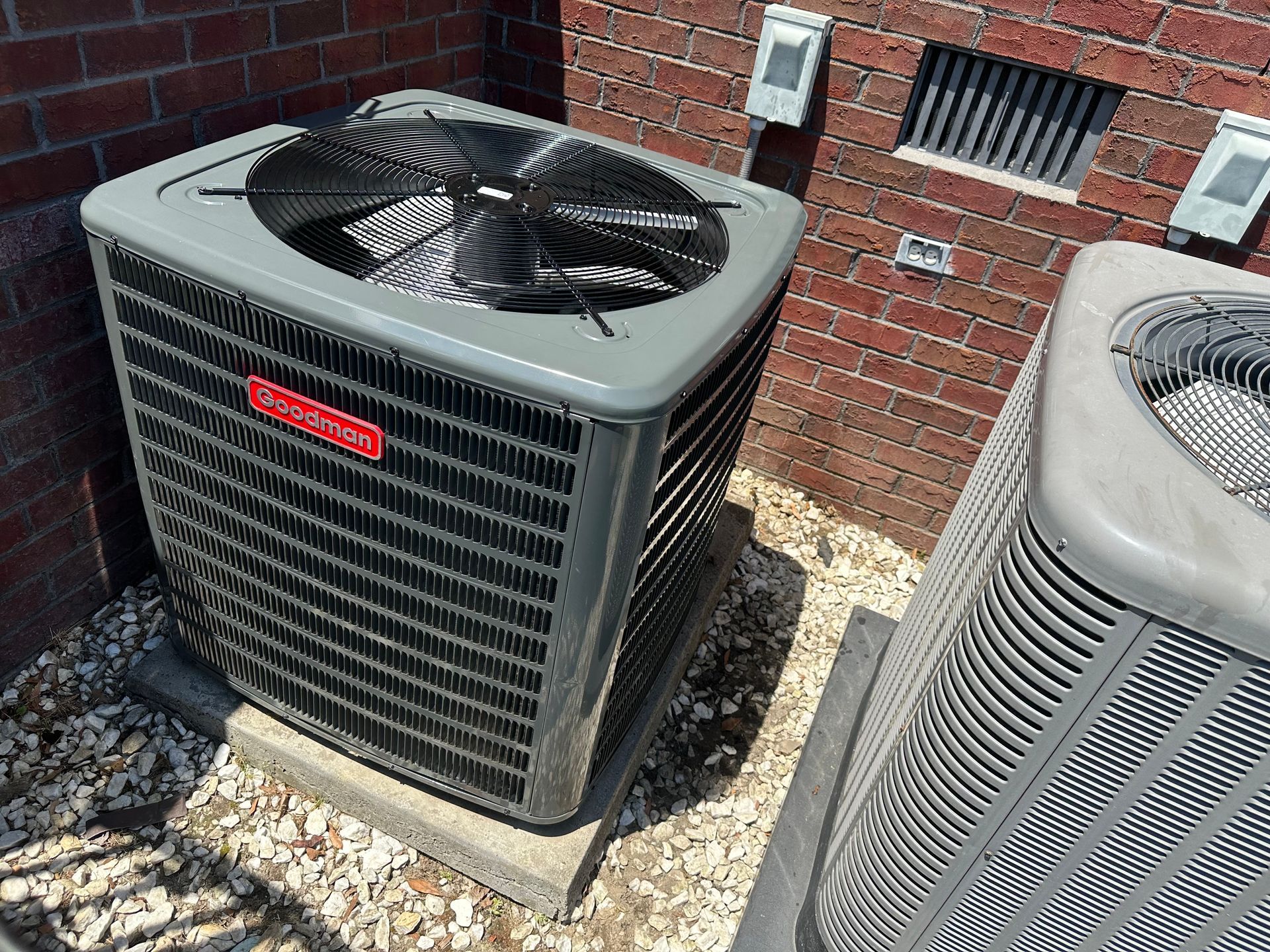 Two air conditioners are sitting outside of a brick building.