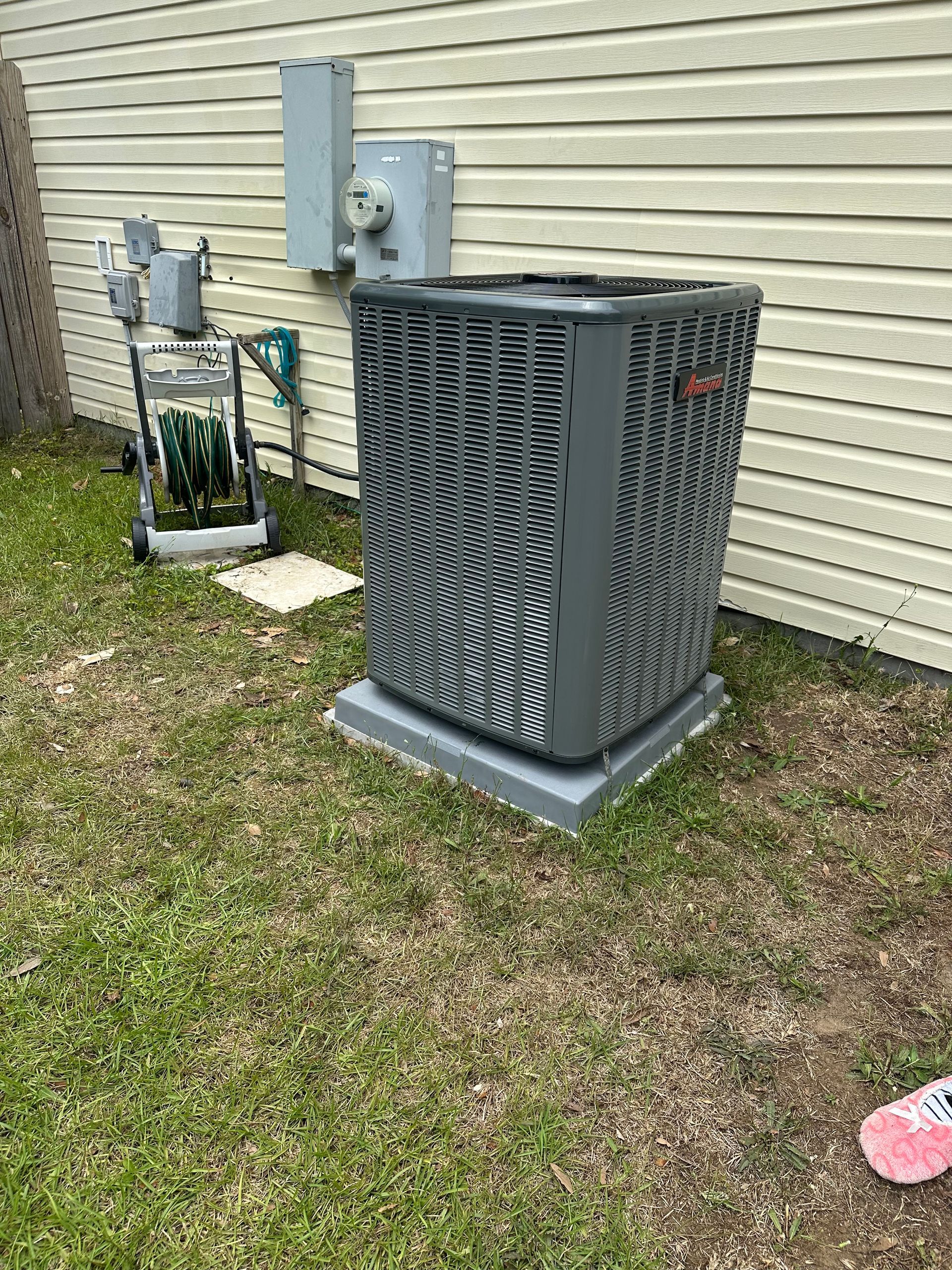 A large air conditioner is sitting in the grass in front of a house.