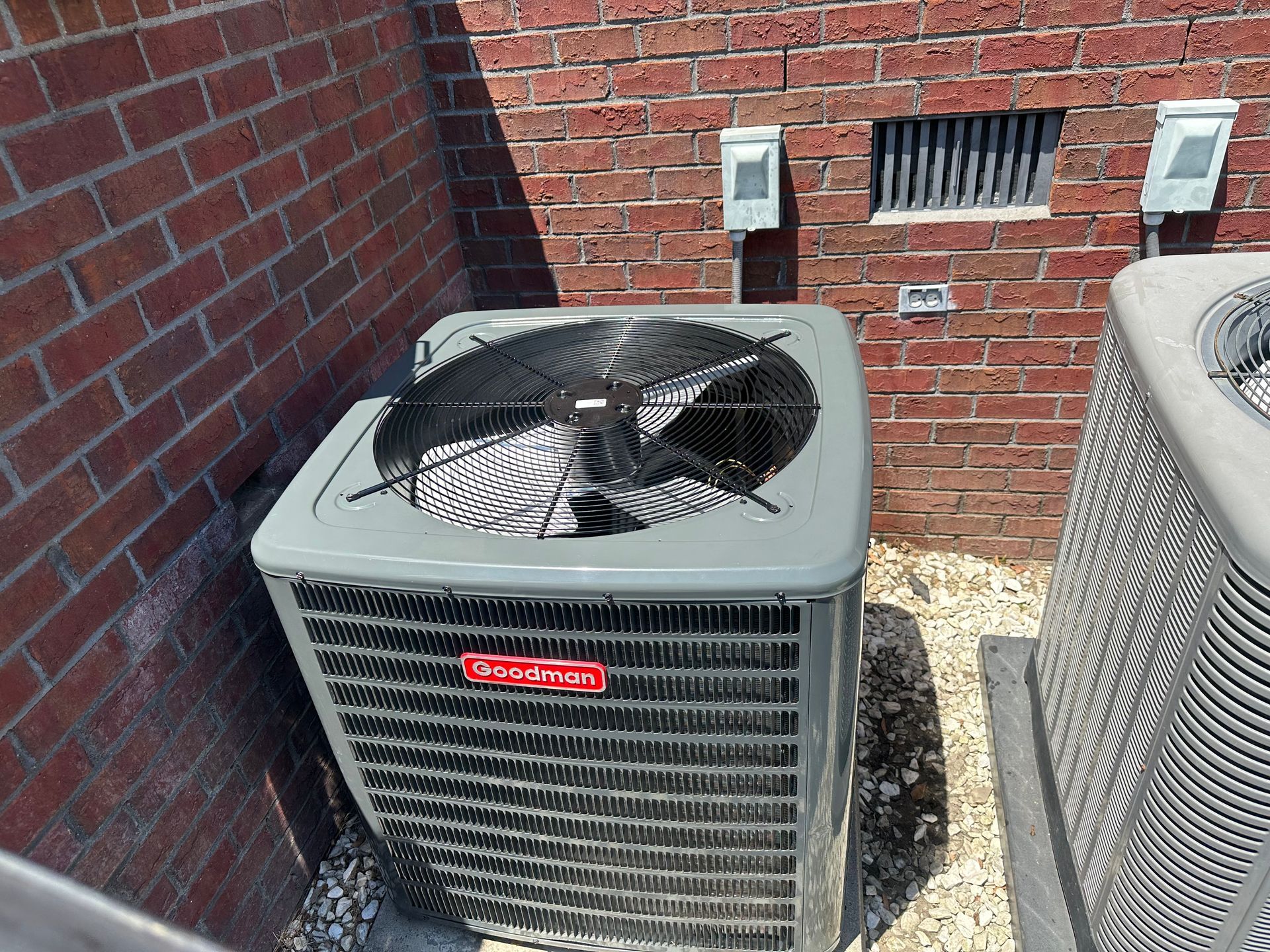 Two air conditioners are sitting next to each other on the side of a brick building.