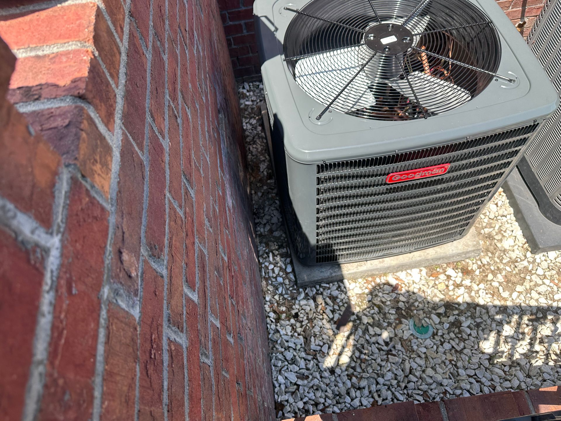 A gray air conditioner is sitting next to a brick wall.