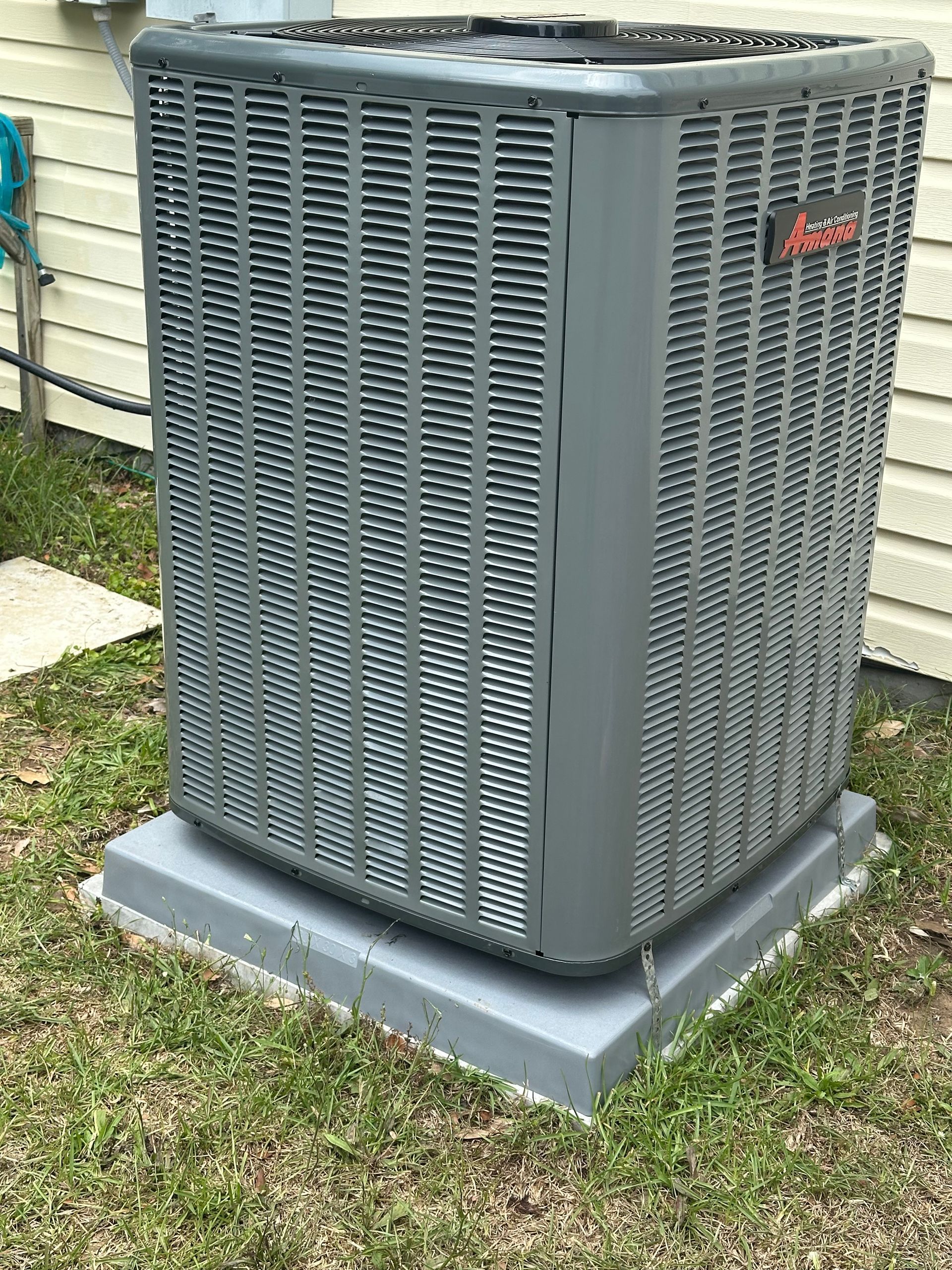 A large air conditioner is sitting on top of a concrete base in the grass.