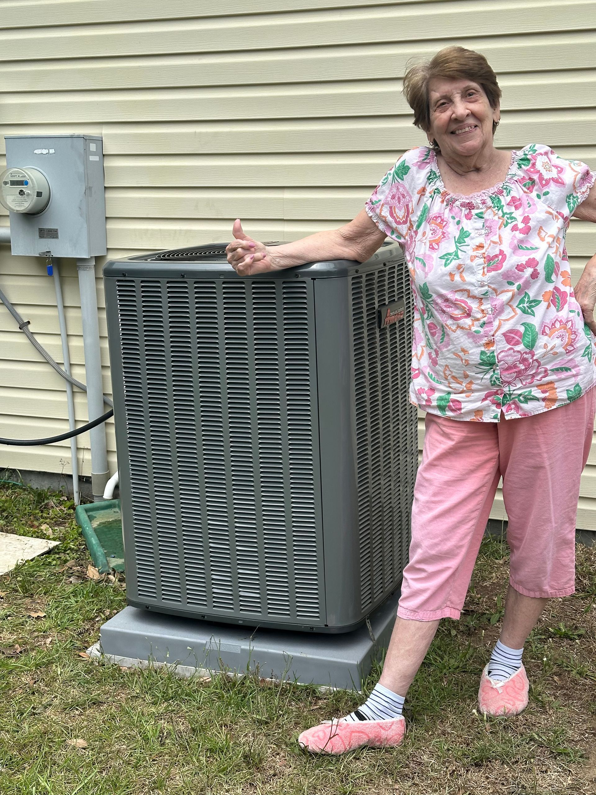 An elderly woman is standing next to a large air conditioner.