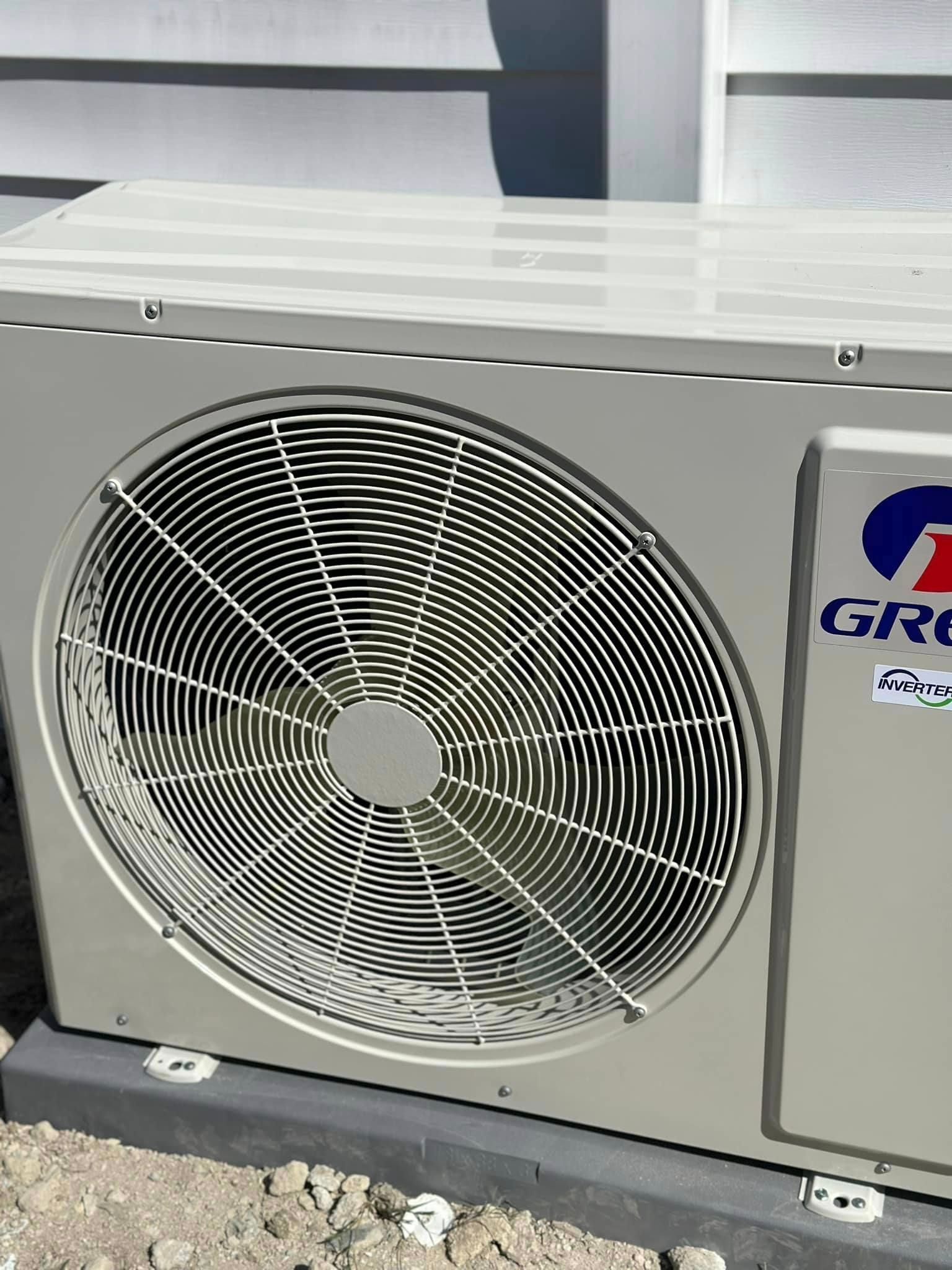 A gree air conditioner is sitting on the ground outside
